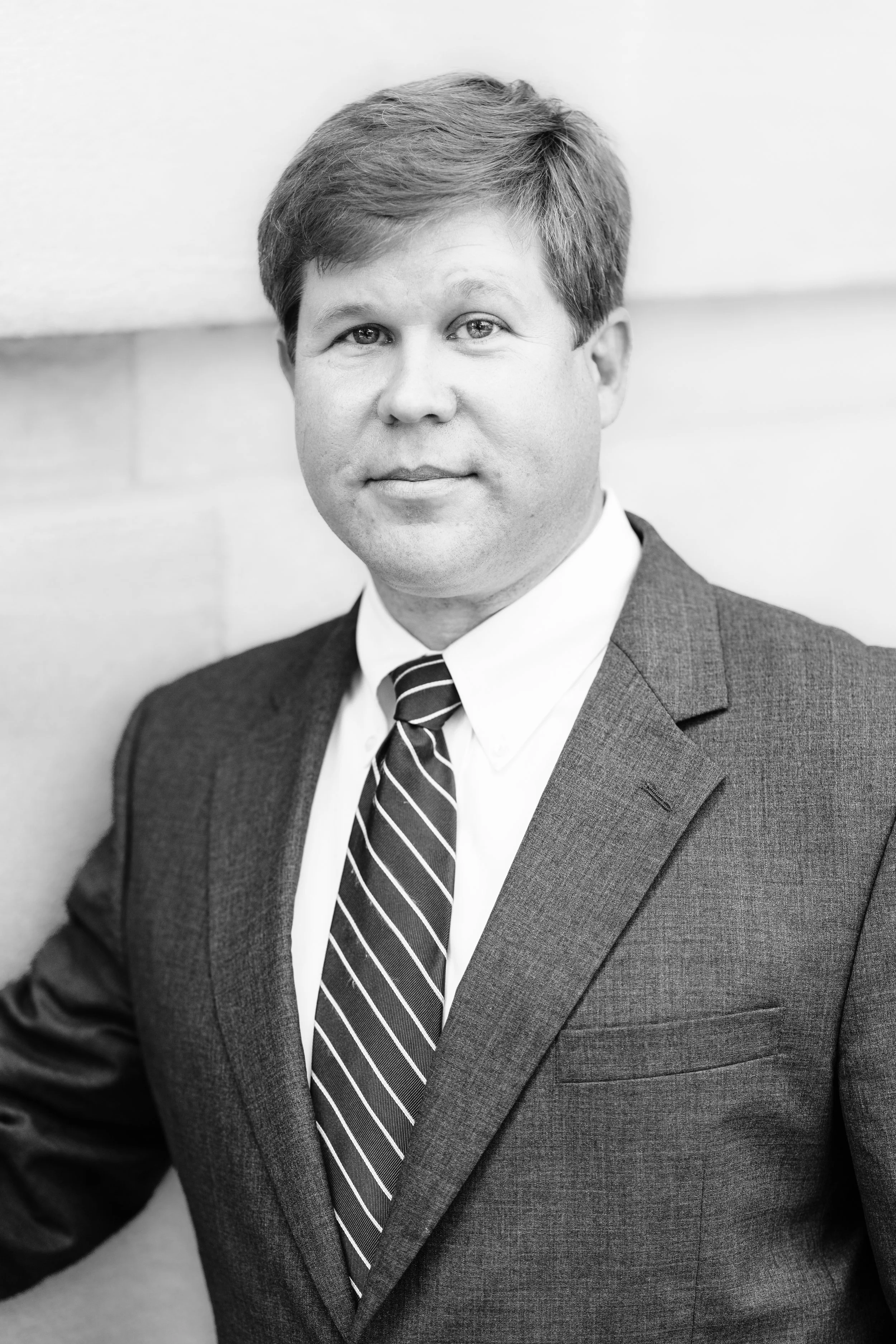 Black and white headshot of a man in a suit and striped tie