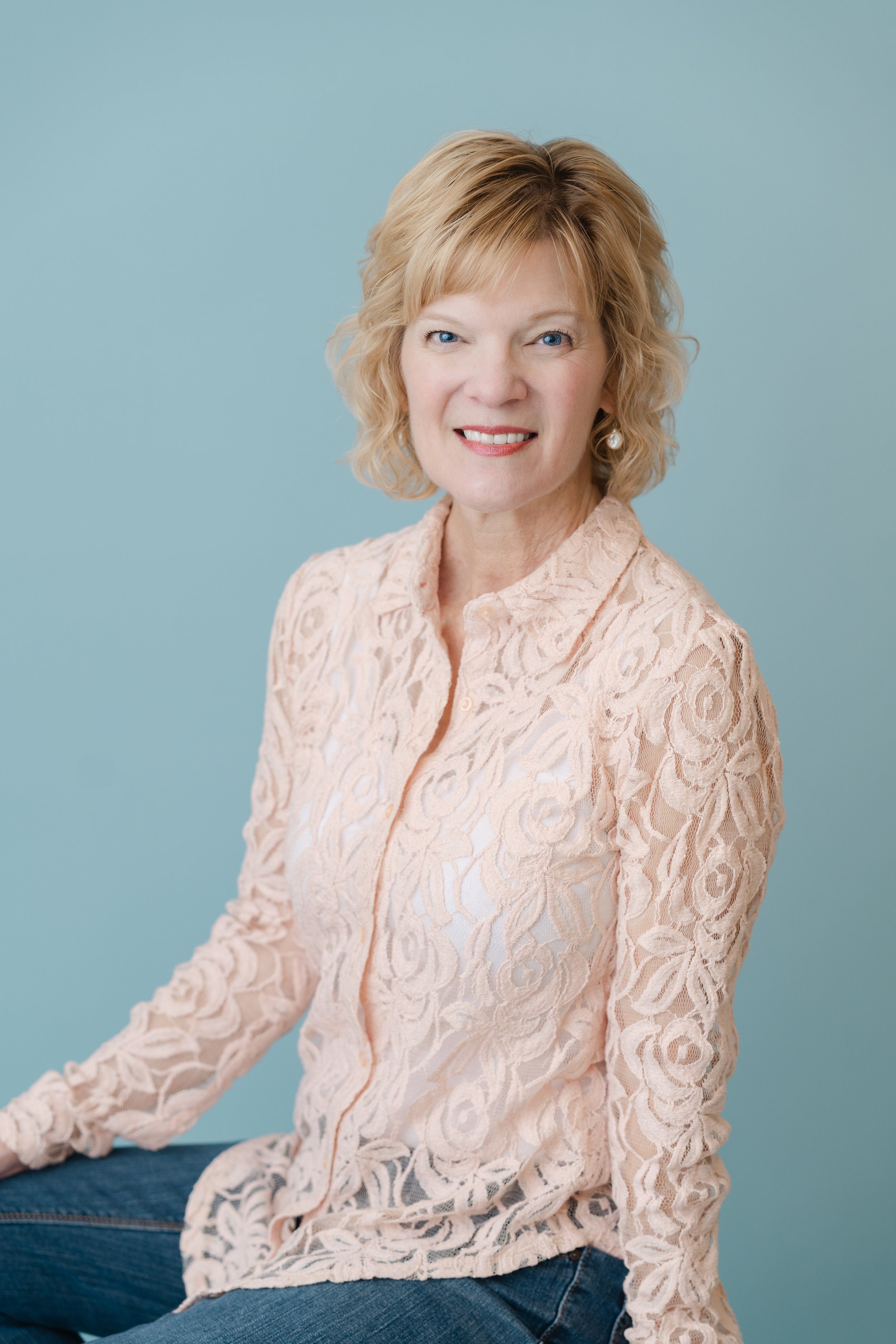 Branding portrait of a smiling woman with short blonde hair in a peach lace blouse against a teal background
