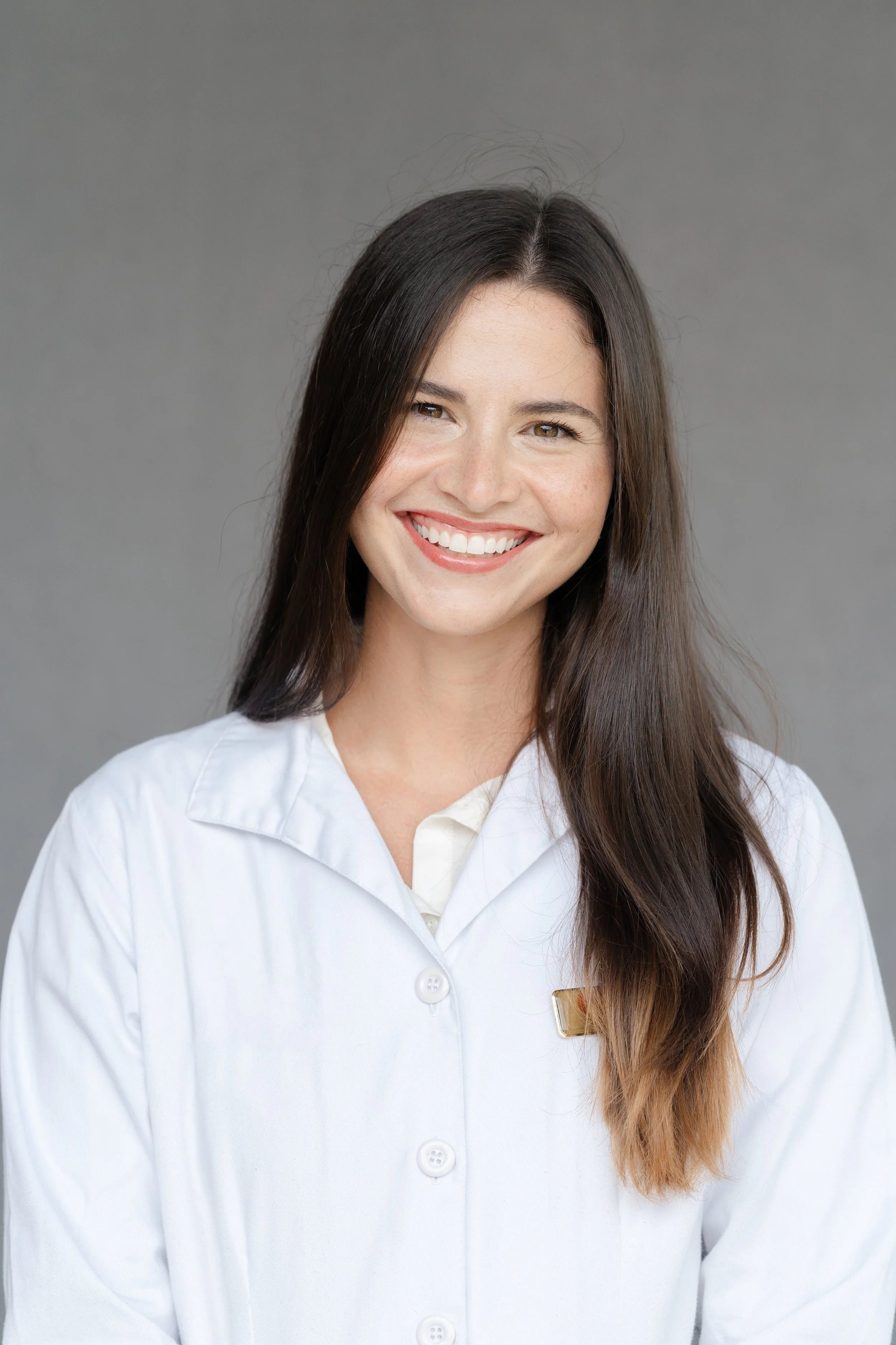 Professional headshot of a smiling woman with long dark hair in a white lab coat