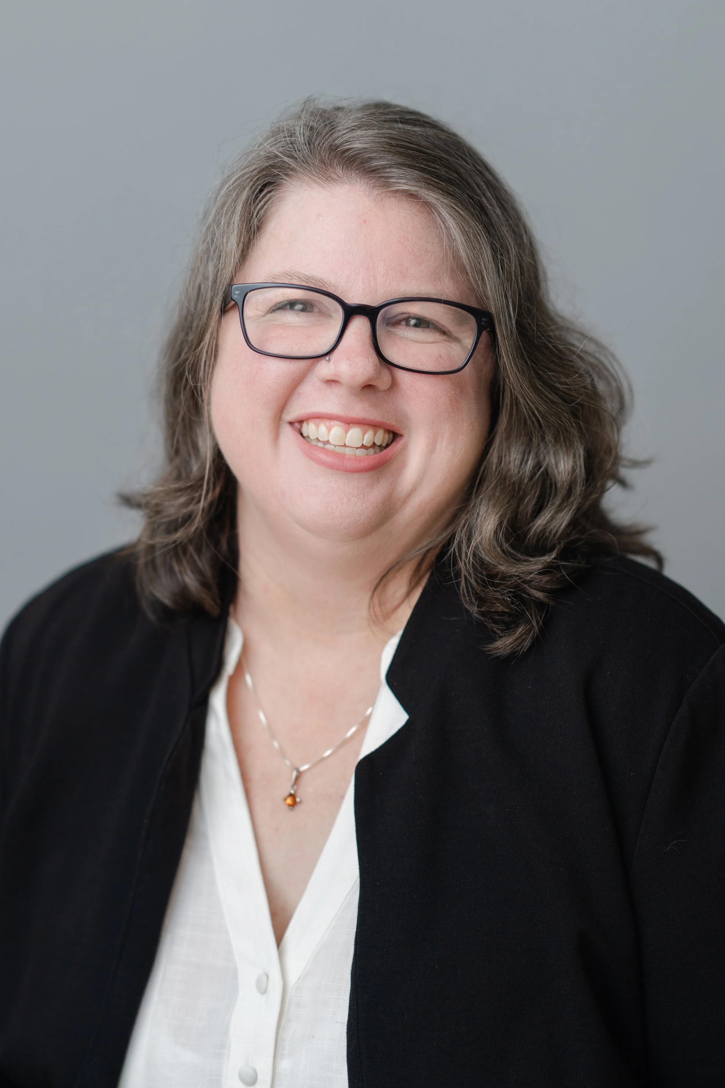 Professional headshot of a smiling woman with glasses in a black blazer and white top