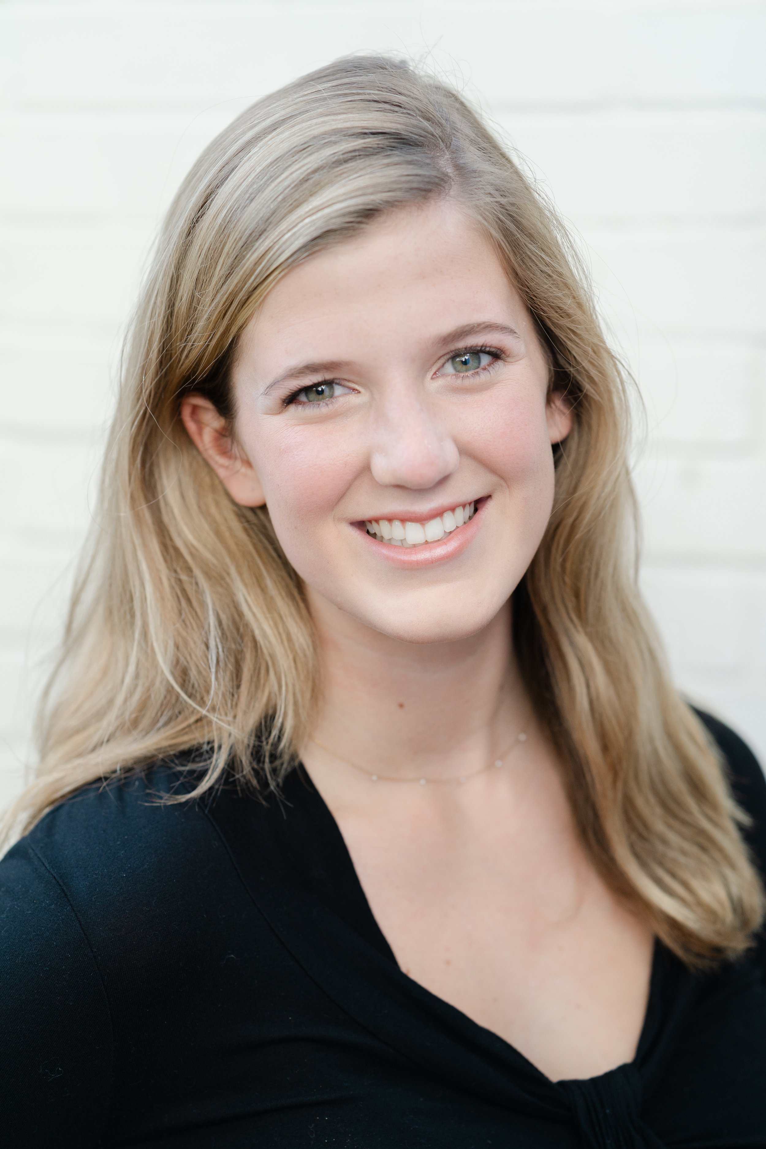 Professional headshot of a smiling woman with long blonde hair in a black top