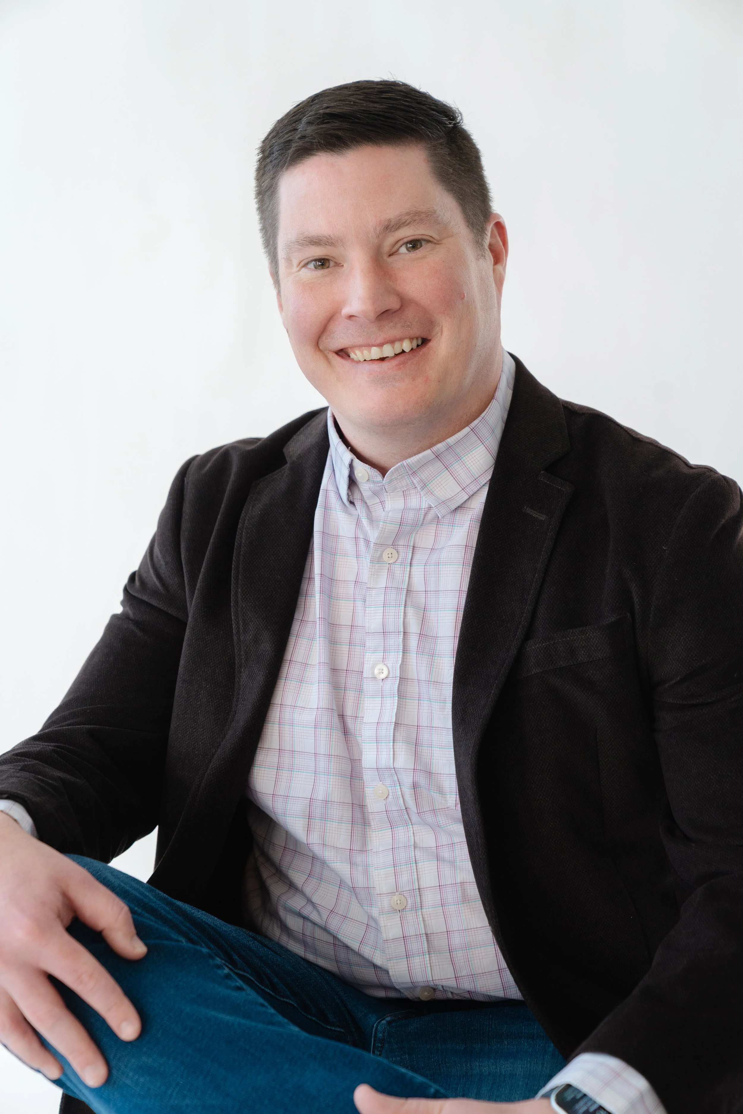 Professional headshot of a smiling man in a dark blazer and checked shirt