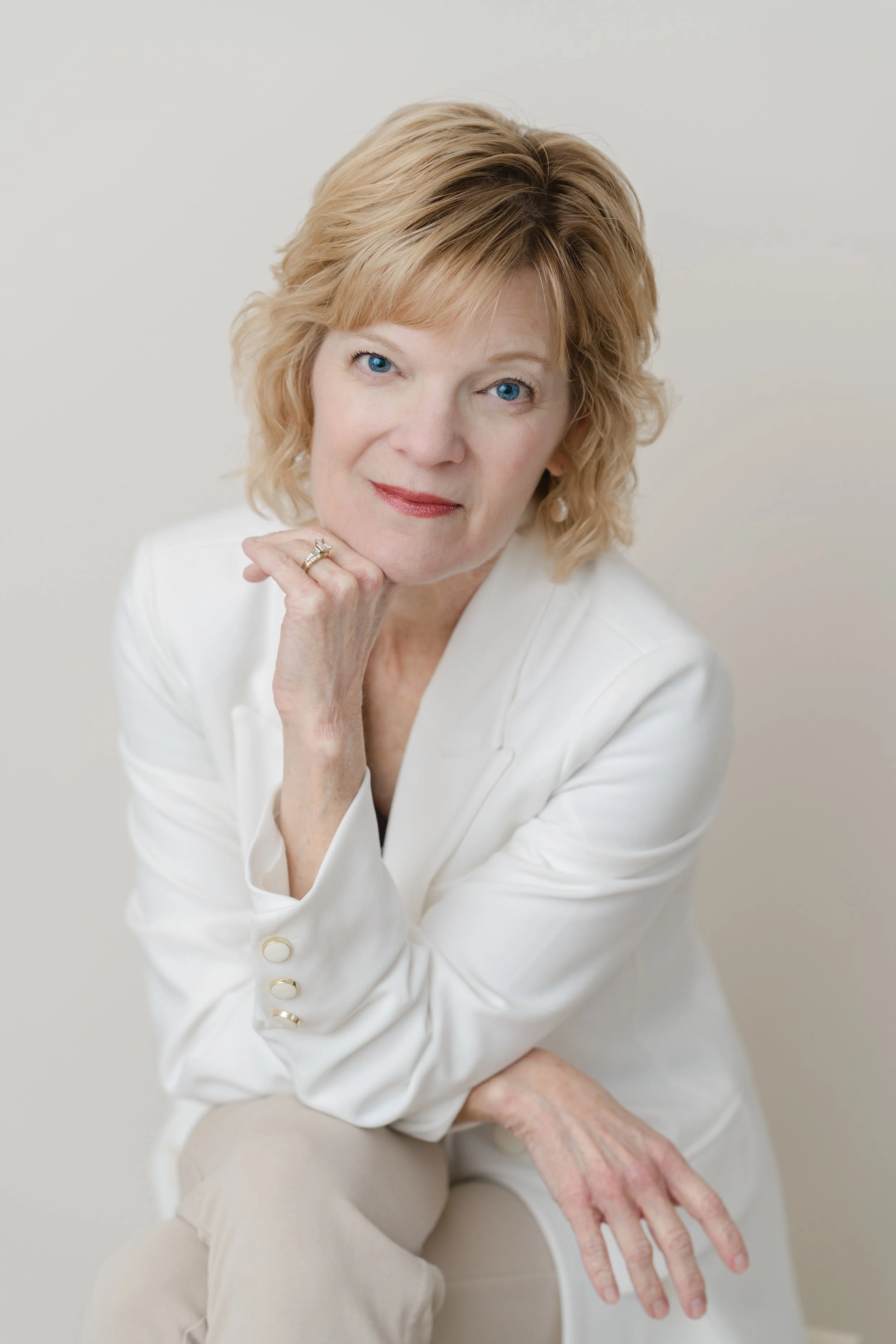 Branding portrait of a woman with short blonde hair in a white blazer, resting her chin on her hand