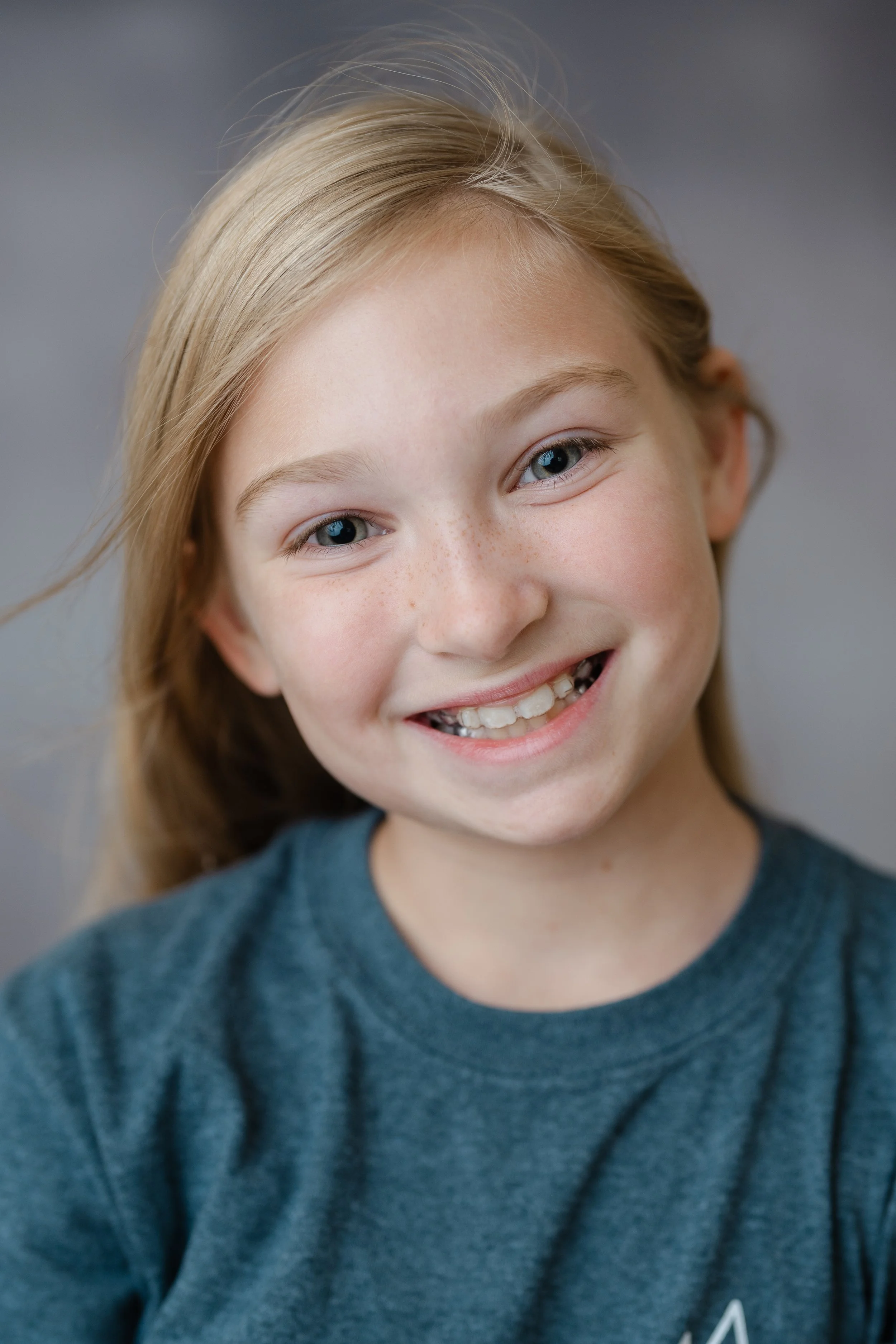 School portrait of a smiling girl with long blonde hair in a teal T-shirt