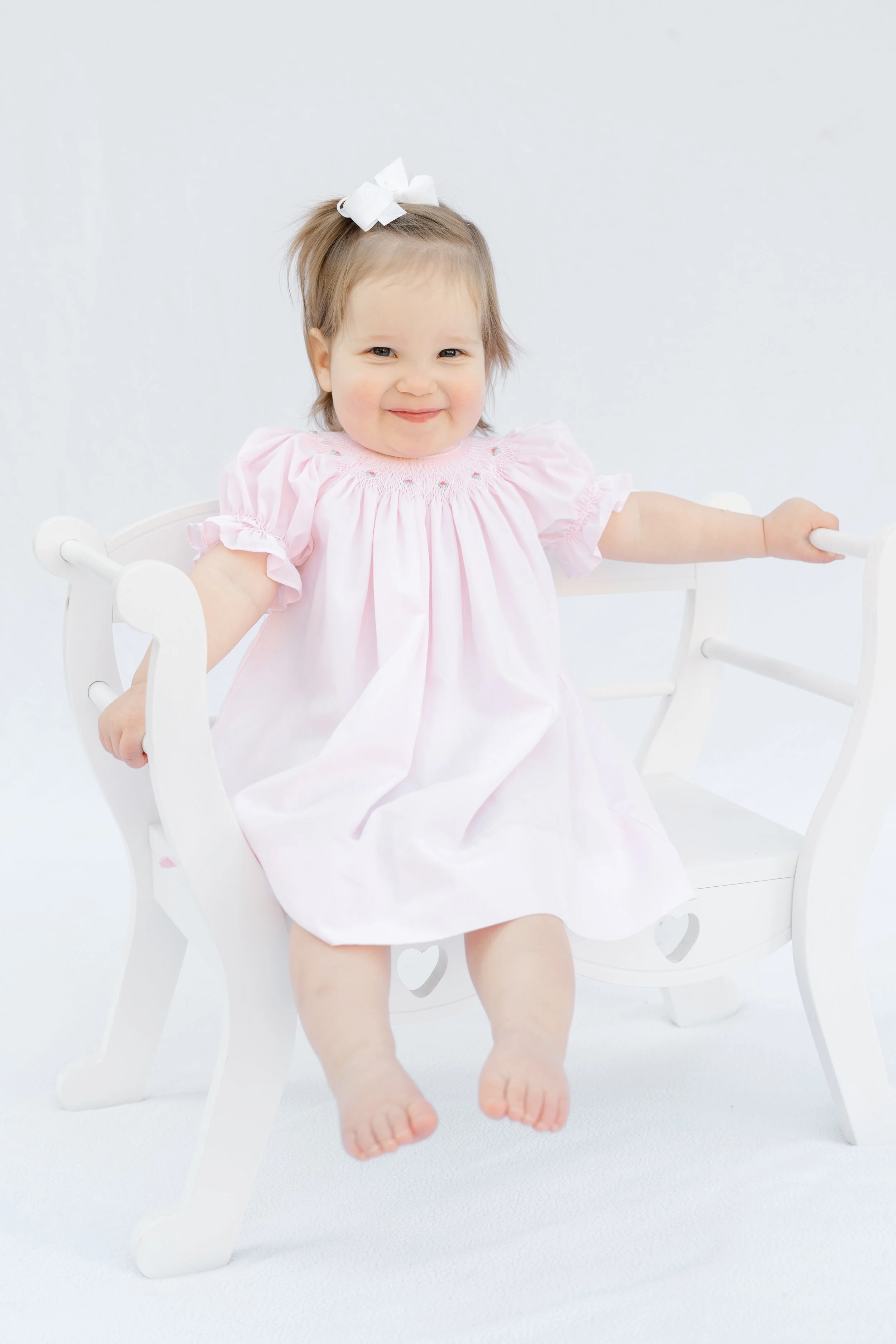 Portrait of a baby girl in a pink dress sitting on a white chair