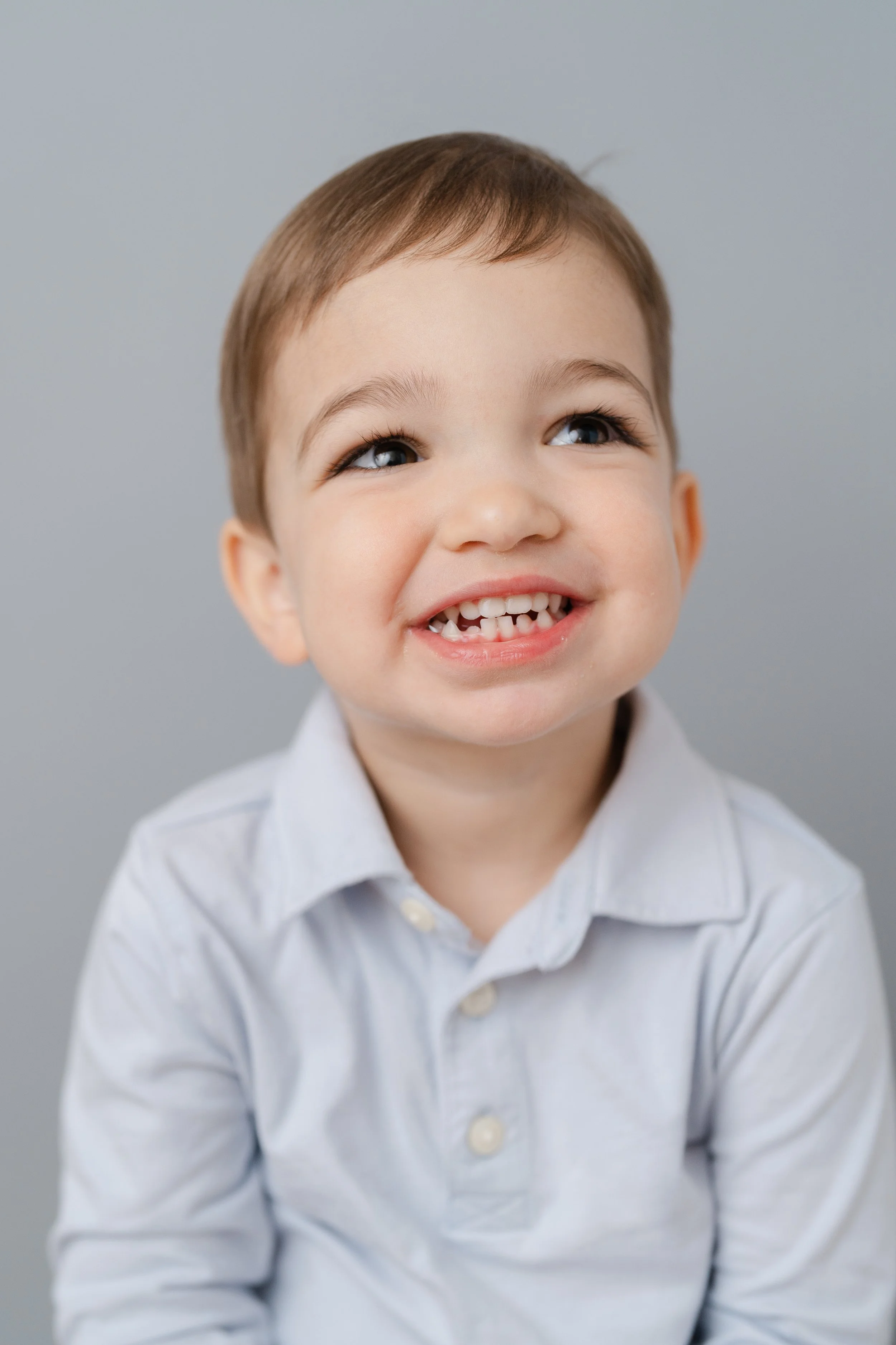 Portrait of a laughing little boy in a light gray collared shirt
