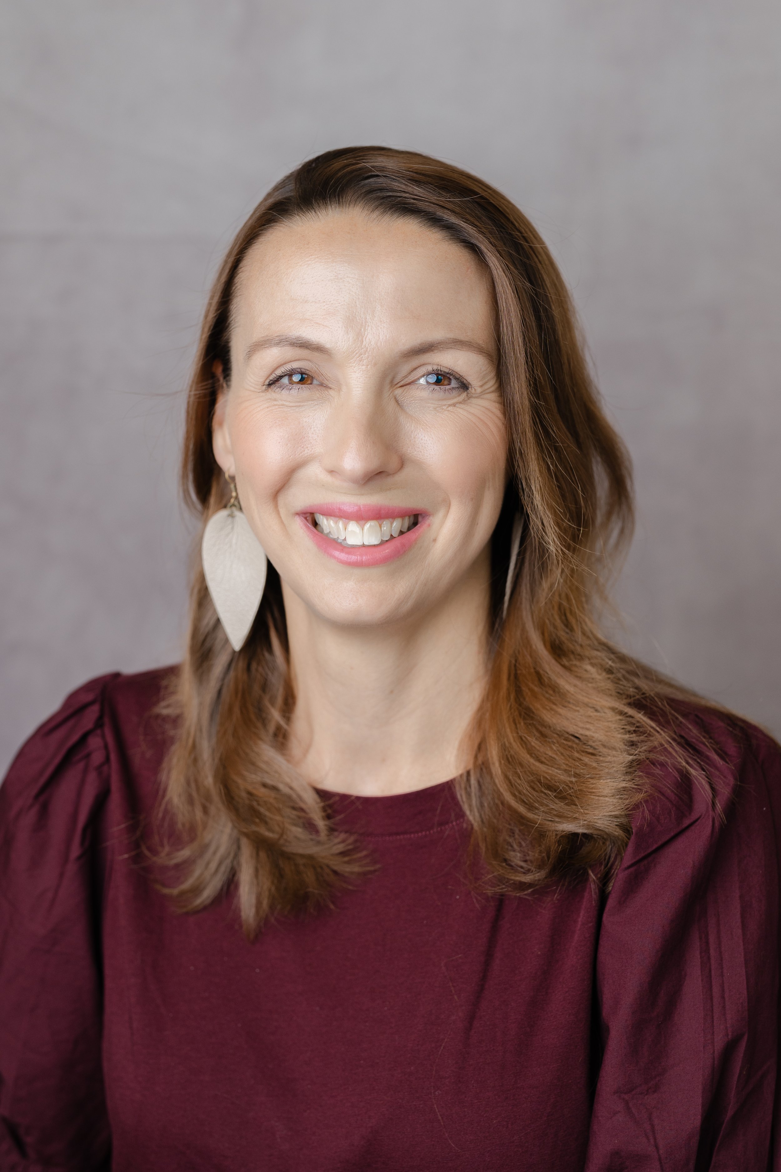 Professional headshot of a smiling woman with shoulder-length brown hair in a burgundy top