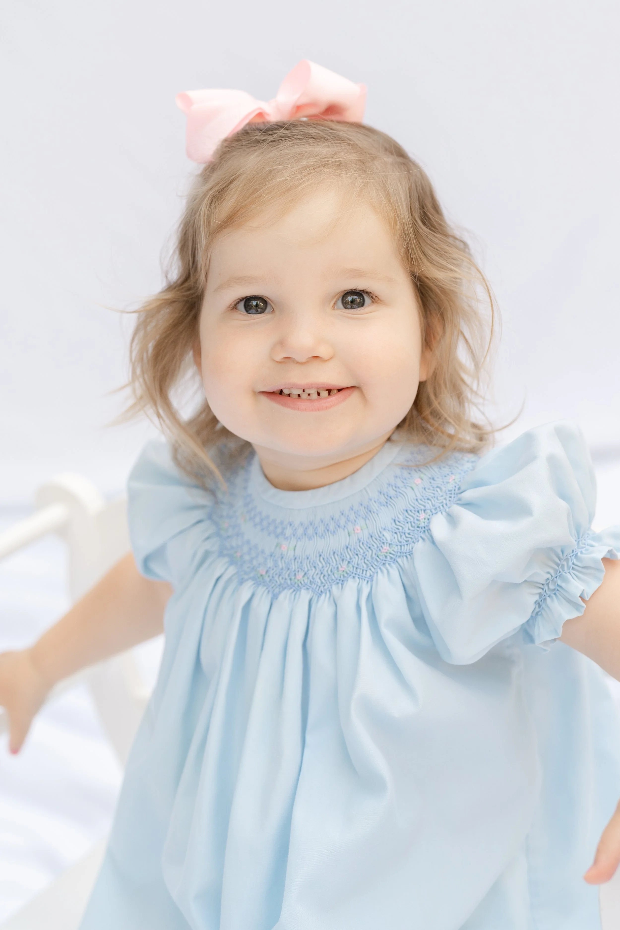 Portrait of a toddler girl with a pink bow in a light blue smocked dress