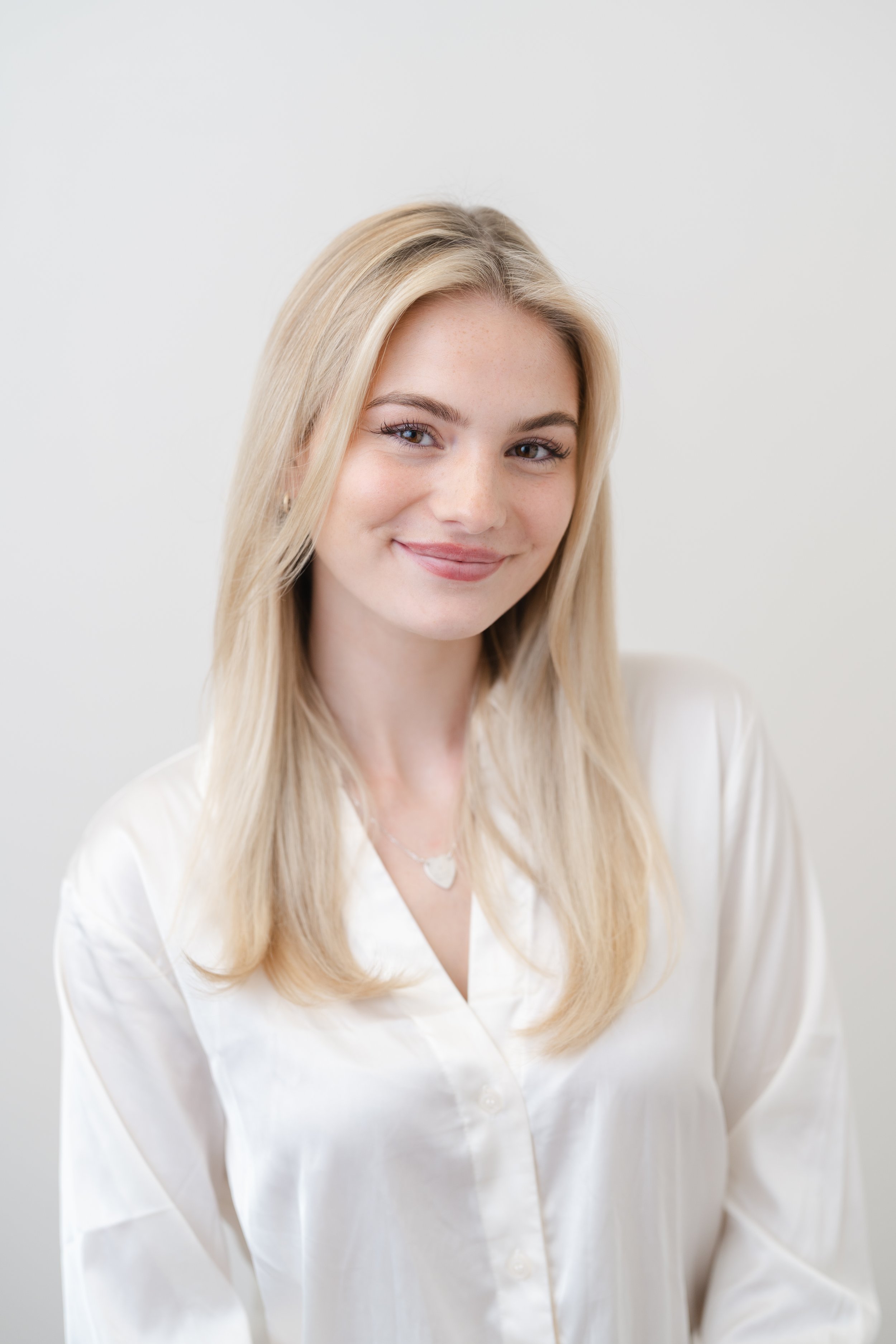 Professional headshot of a young woman with long blonde hair in a white blouse