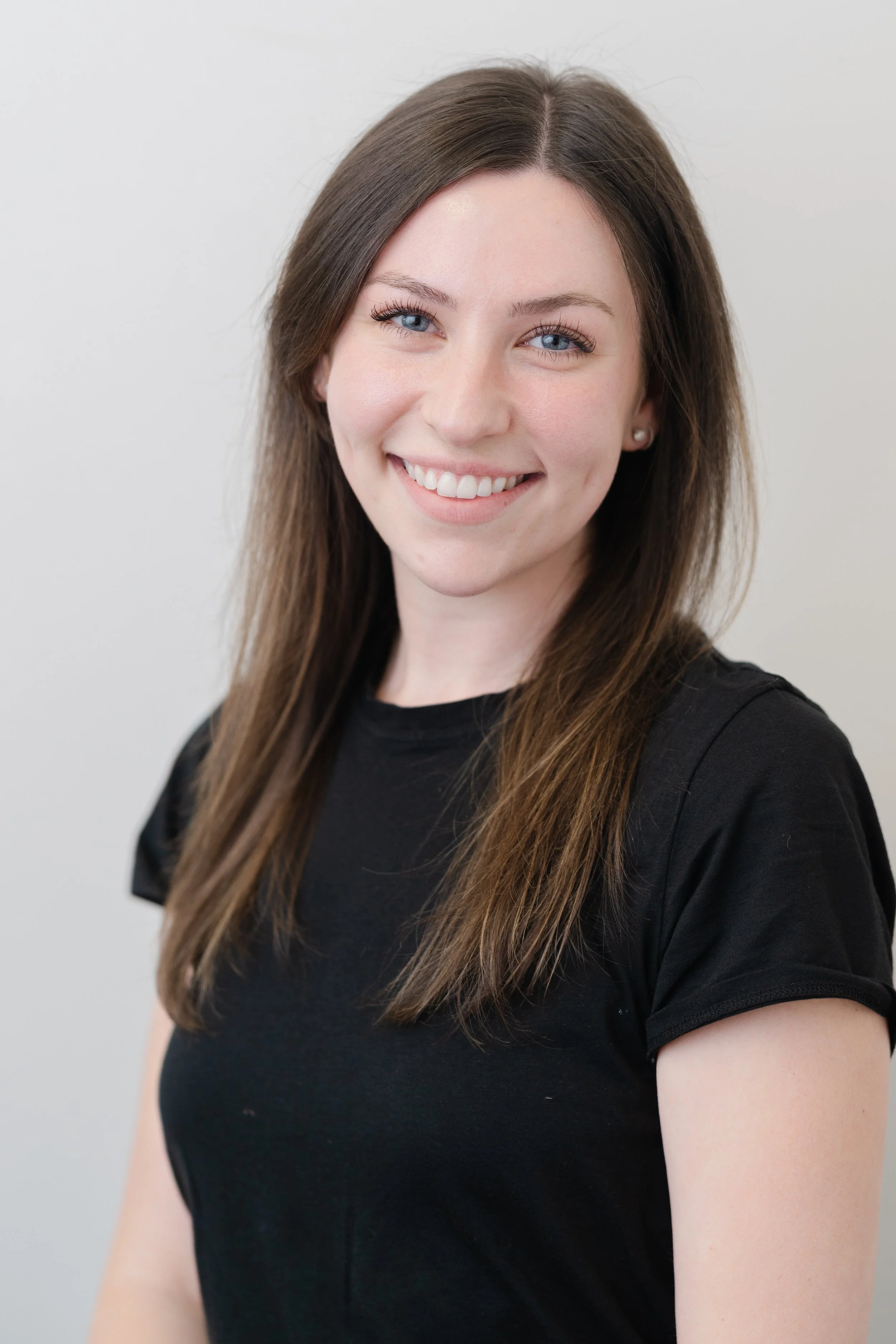 Professional headshot of a smiling woman with long brown hair in a black top