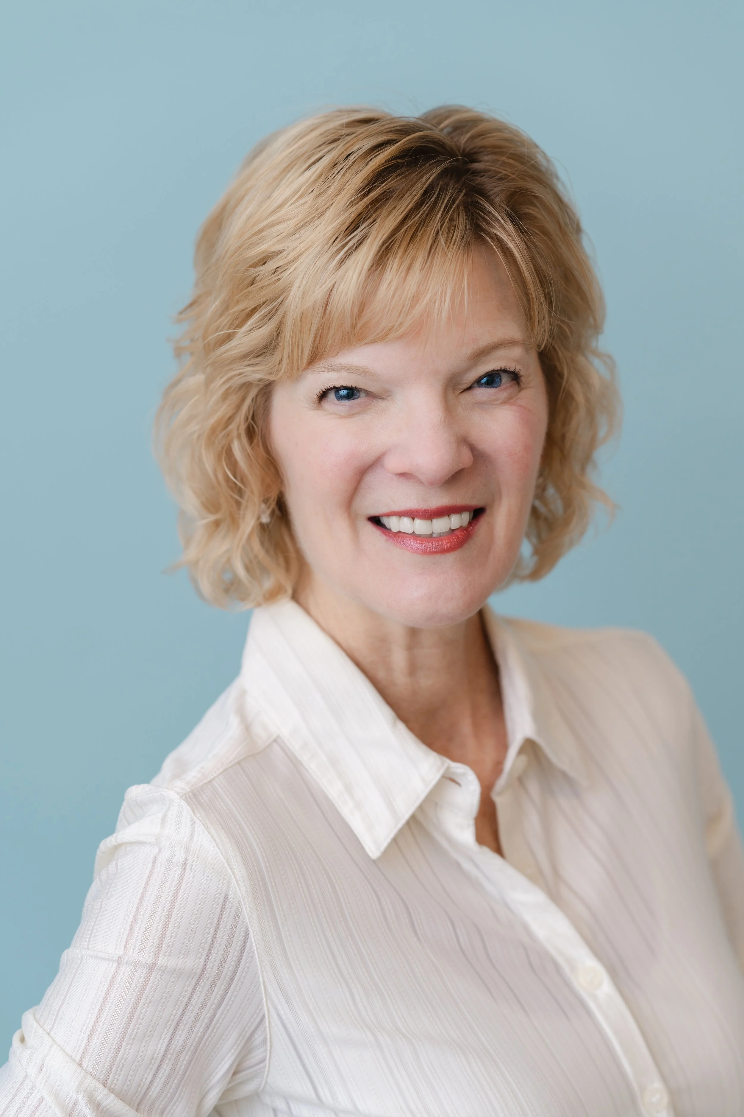 Branding portrait of a smiling woman with short blonde hair in a white blouse against a soft blue background