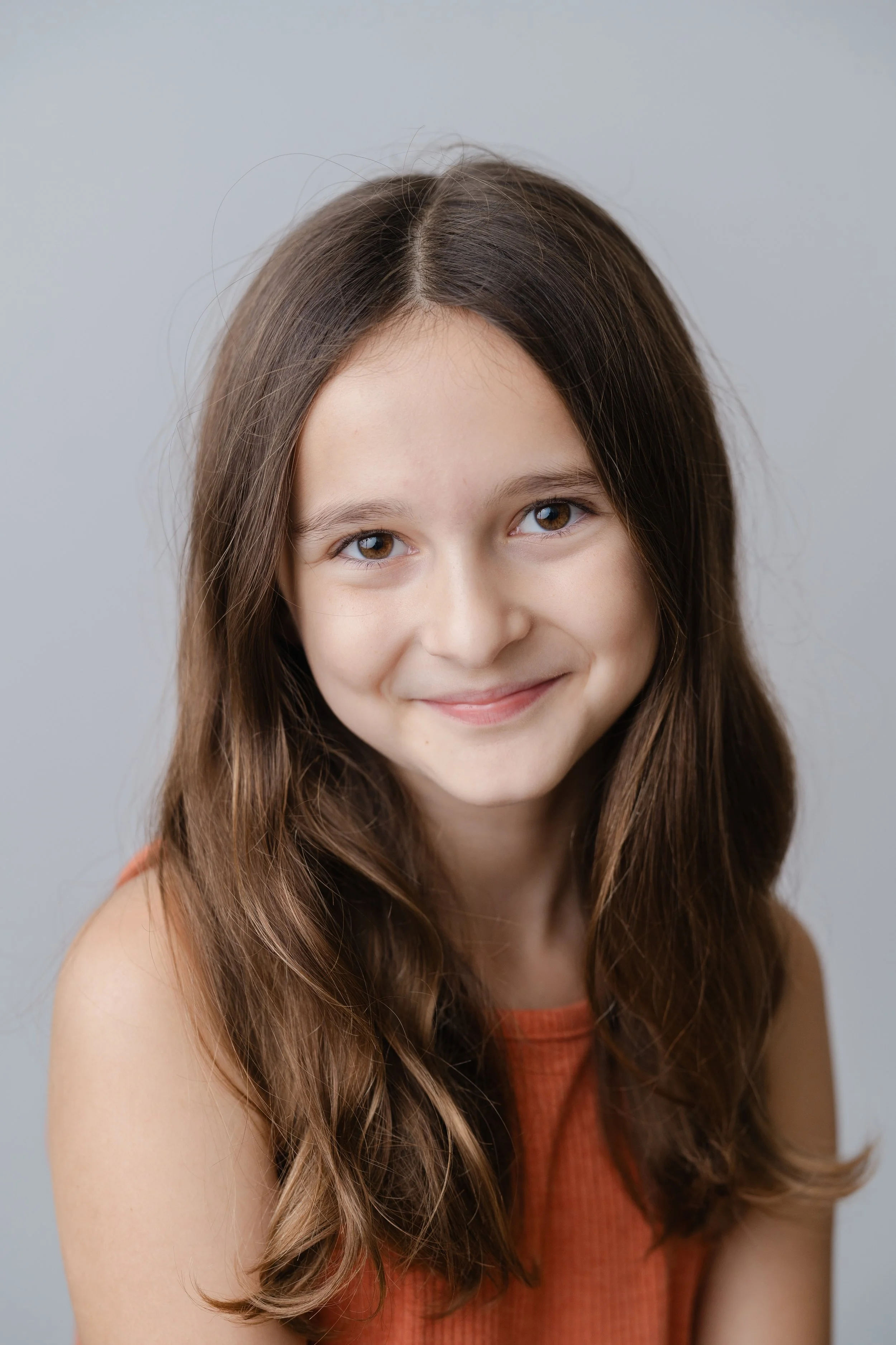 Portrait of a smiling girl with long brown hair in a rust-colored top