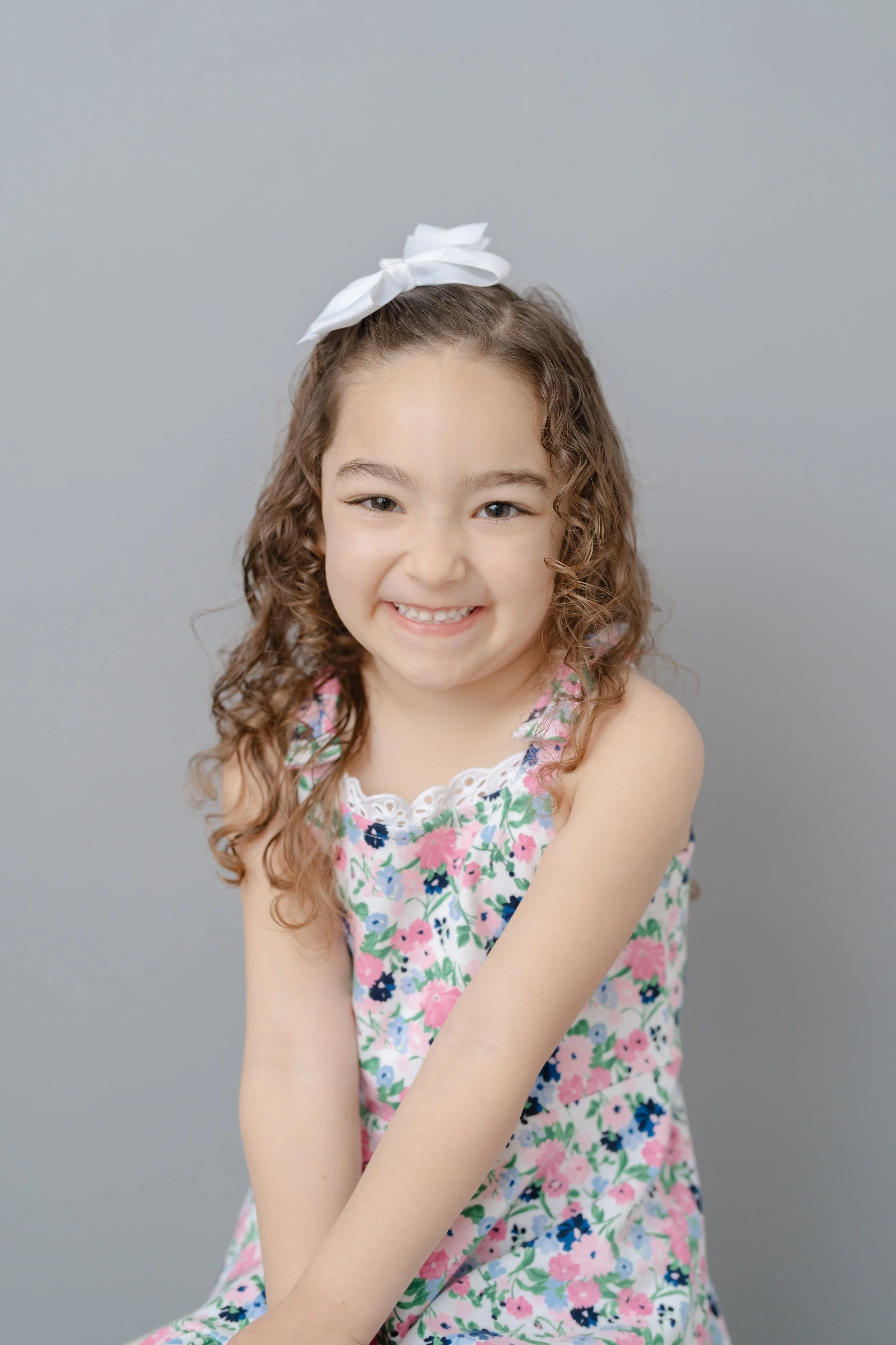 Portrait of a smiling girl with curly hair and a white bow in a floral dress