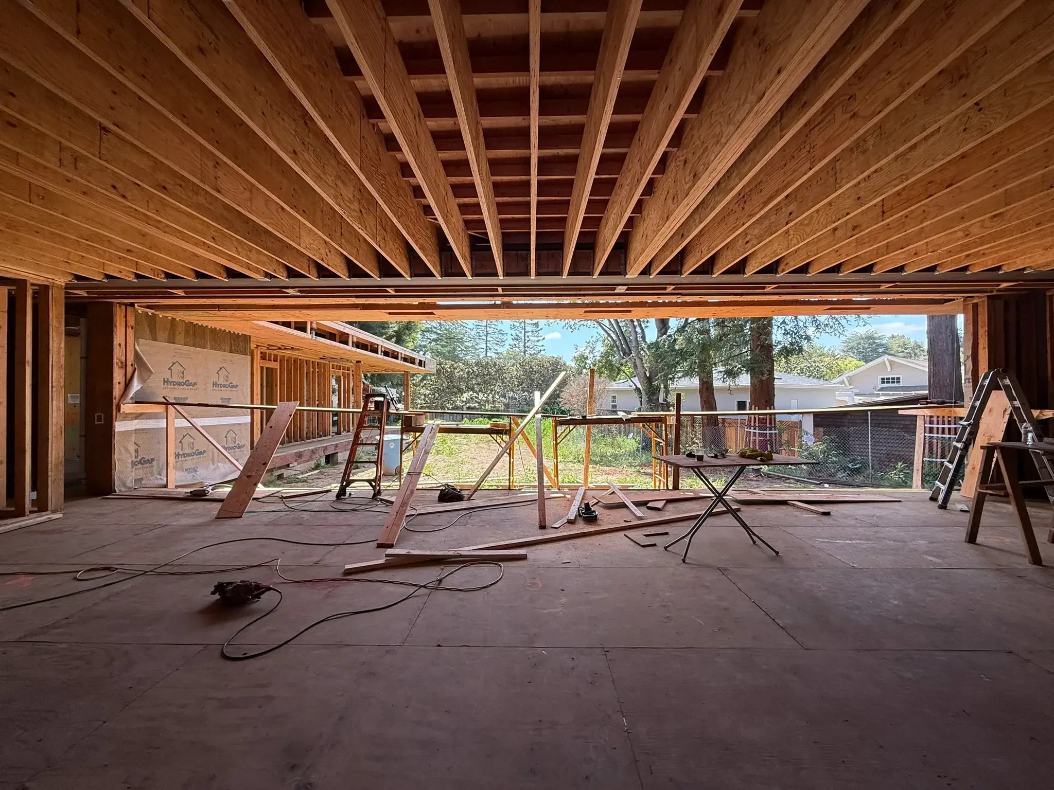 Construction site of a house with exposed wooden framework and open wall to outdoor view, scattered tools, and ladders.