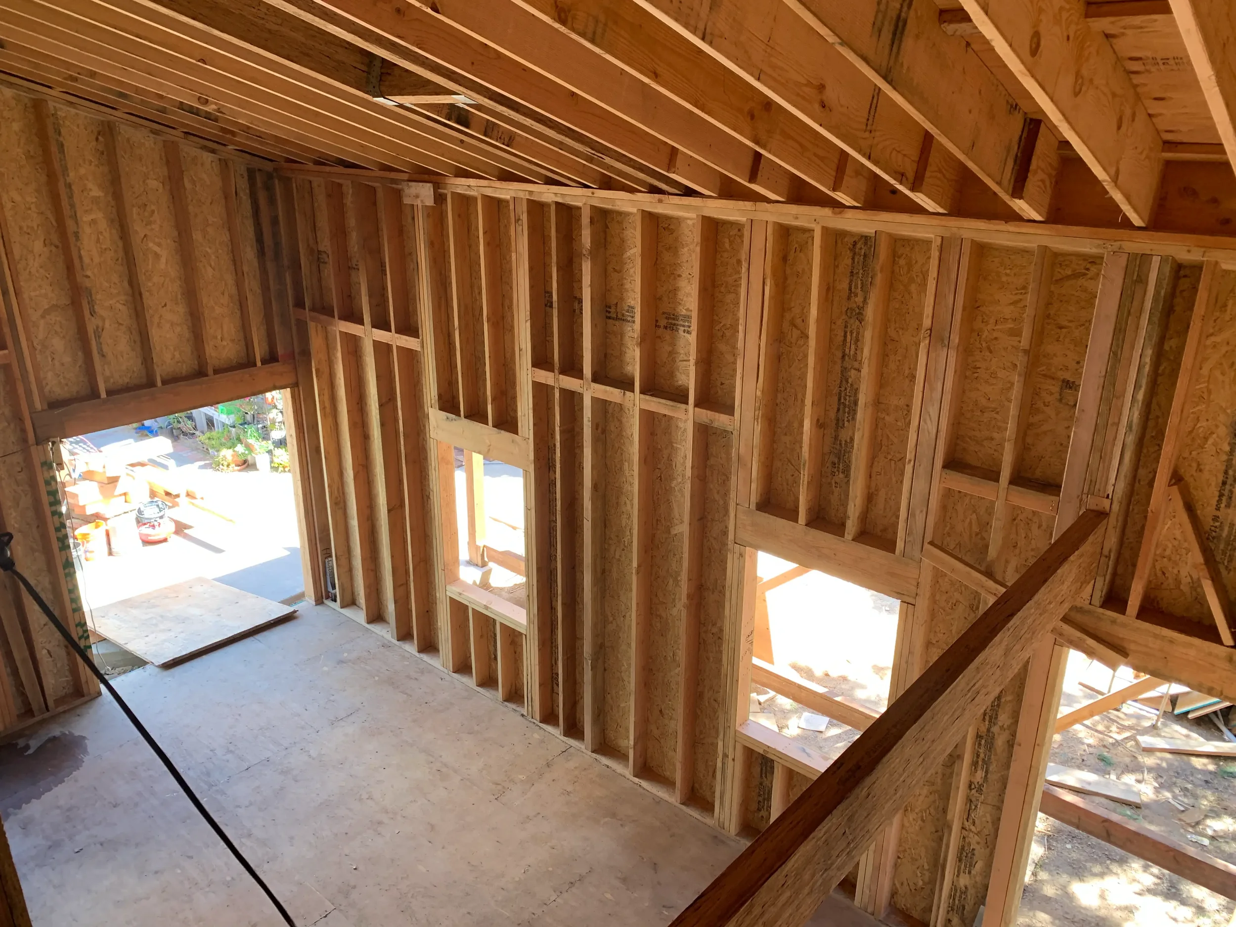 Interior view of a house under construction, showing exposed wooden framing and wall studs.