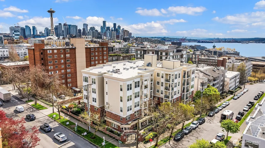Cityscape view of Seattle featuring the Space Needle with modern apartment buildings in the foreground and a river in the distance under a blue sky with clouds.
