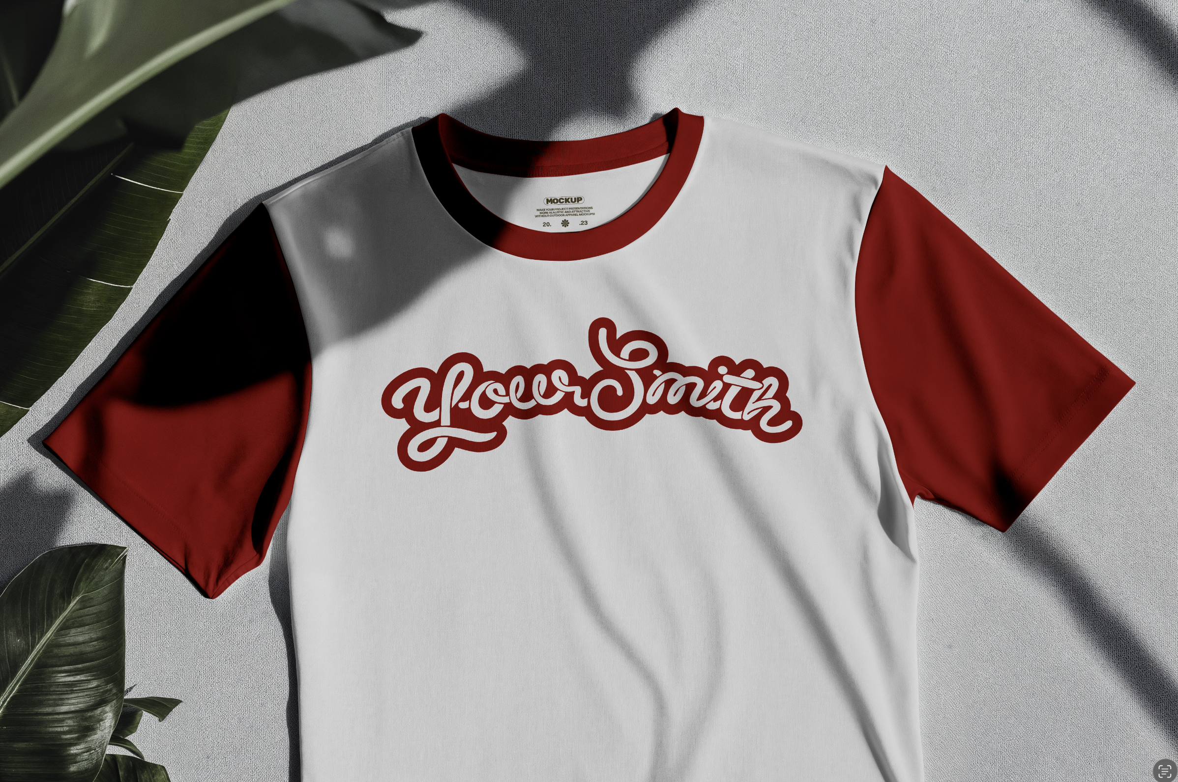 White and red baseball style t-shirt with a red collar and sleeves, laid flat on a light surface, with green leaves around it.