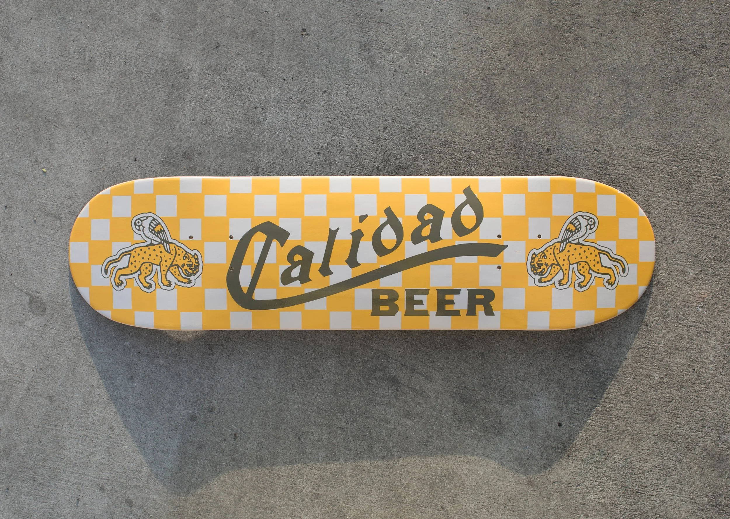 Yellow skateboard deck with a checkered pattern, featuring two illustrated leopards and the text 'Cali' and 'Beer'.