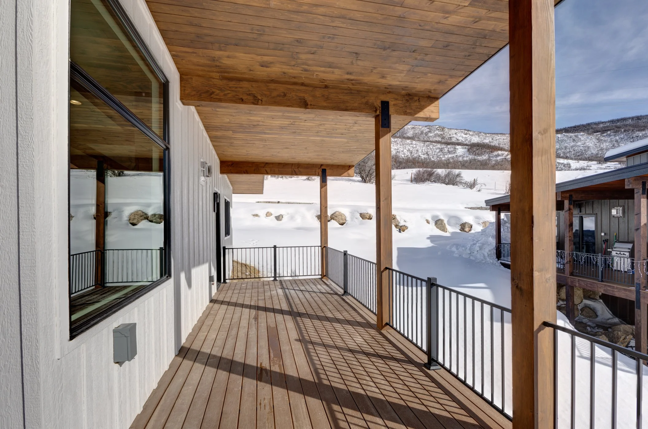Snow-covered landscape viewed from a wooden deck with a roof overhang, wooden posts, and metal railing.