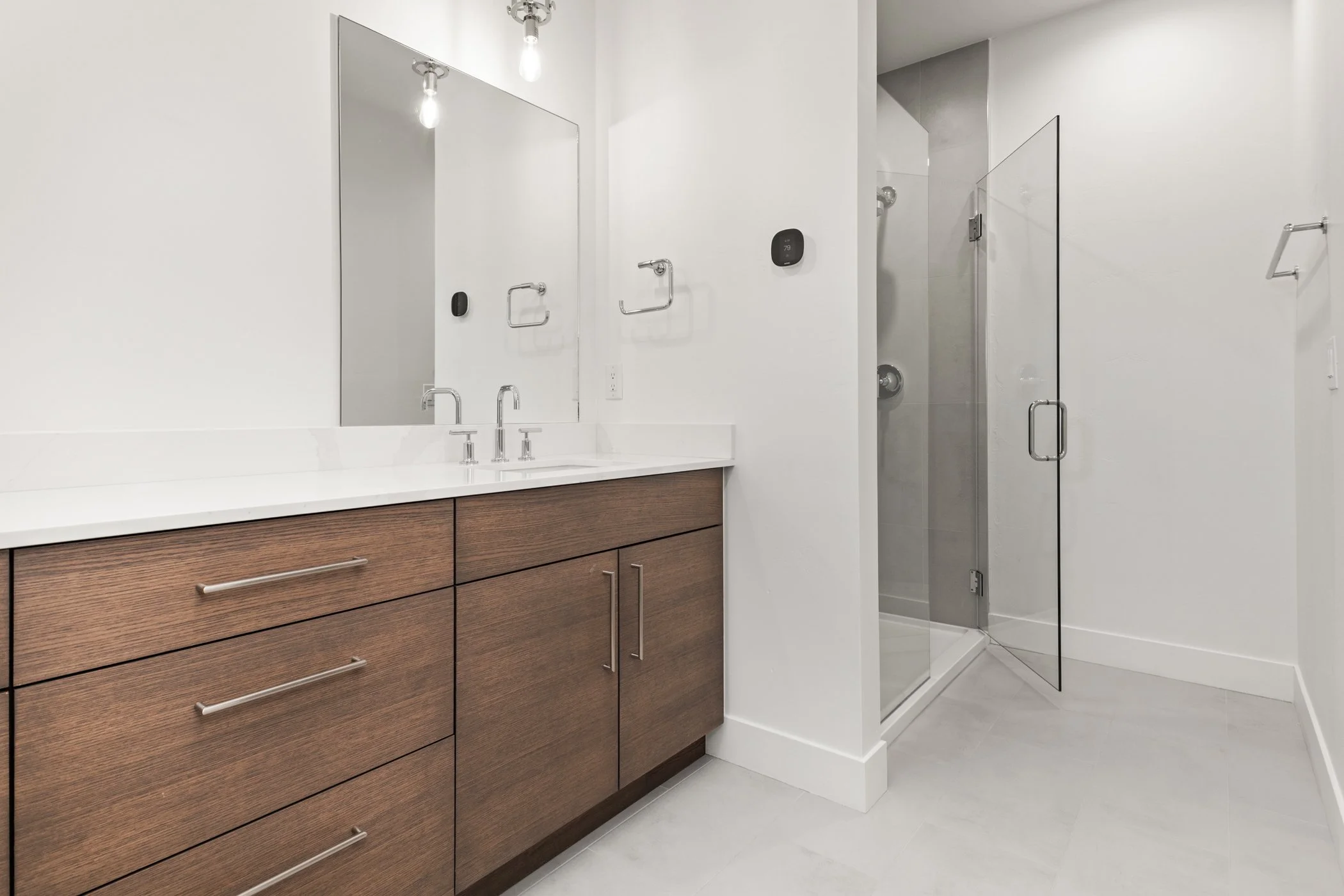 Modern bathroom with wooden vanity, dual sinks, large mirror, and glass shower enclosure.