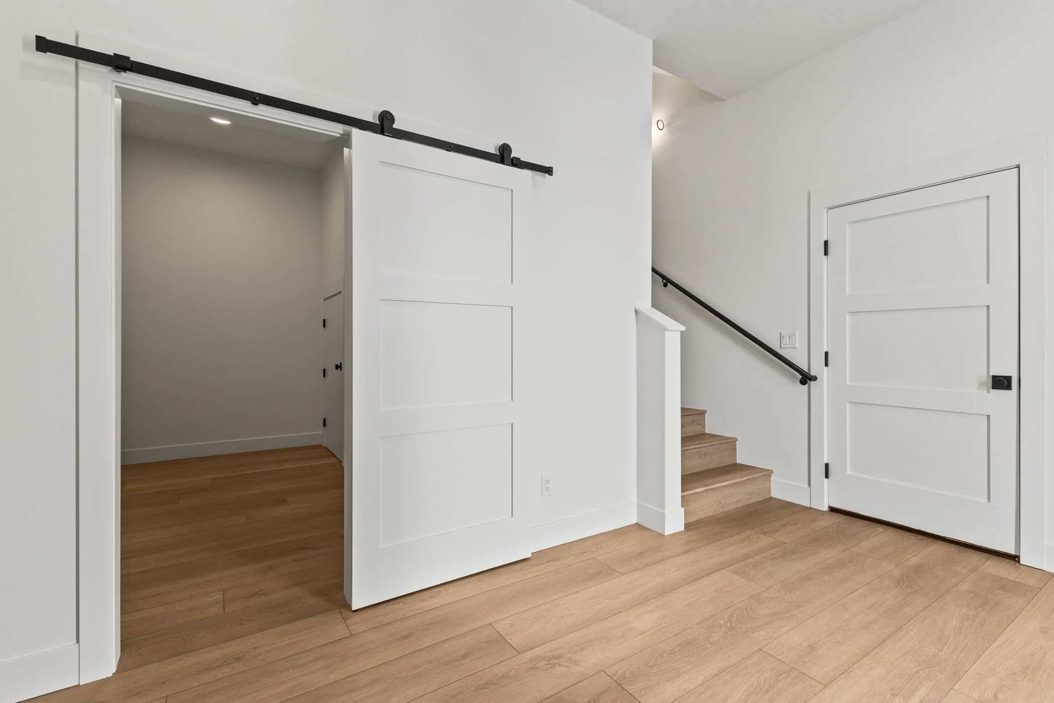 Modern interior with wooden floor, white walls, sliding barn door, staircase, and closet doors.