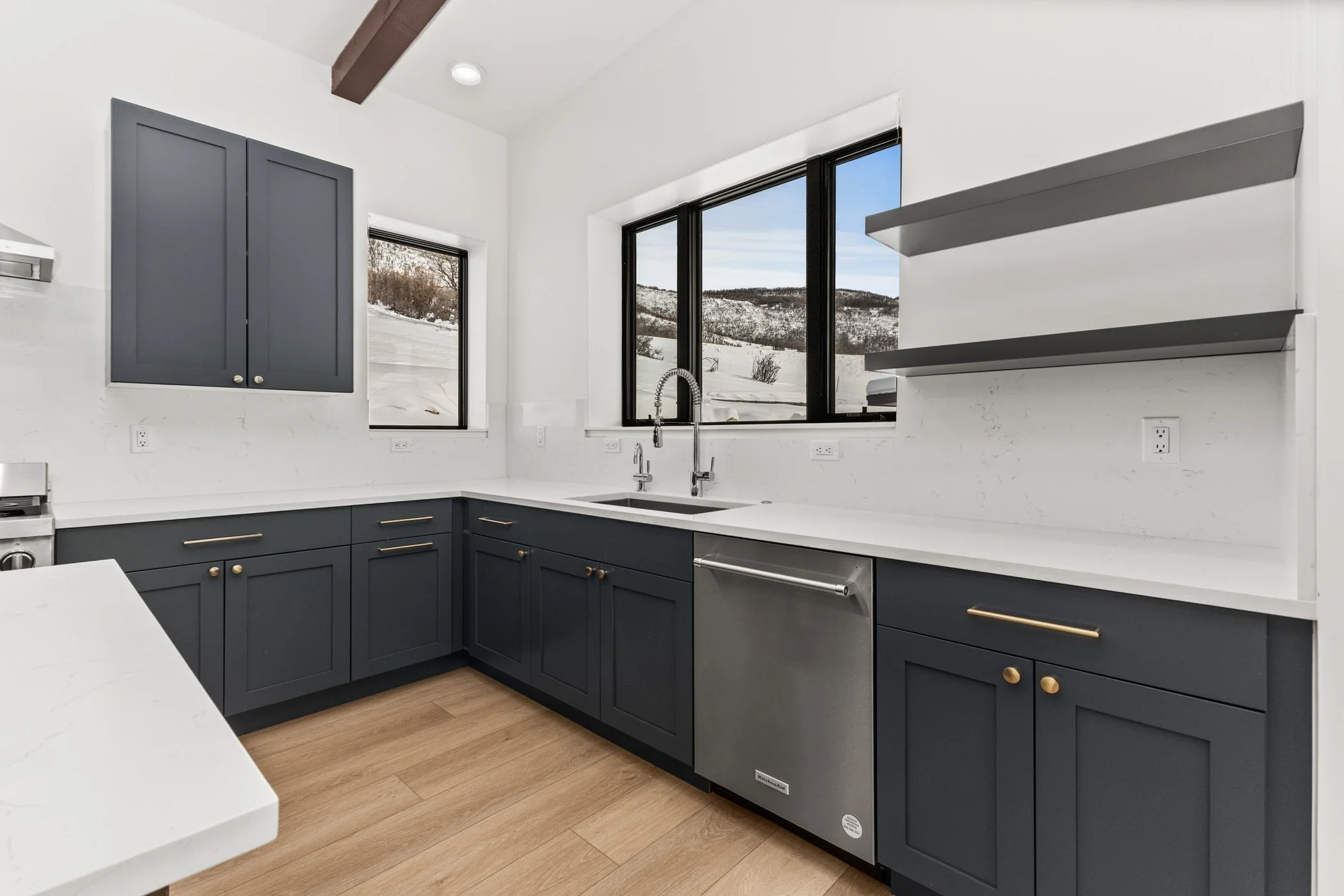 Modern kitchen with dark cabinets, white countertops, stainless steel sink, and wood flooring.