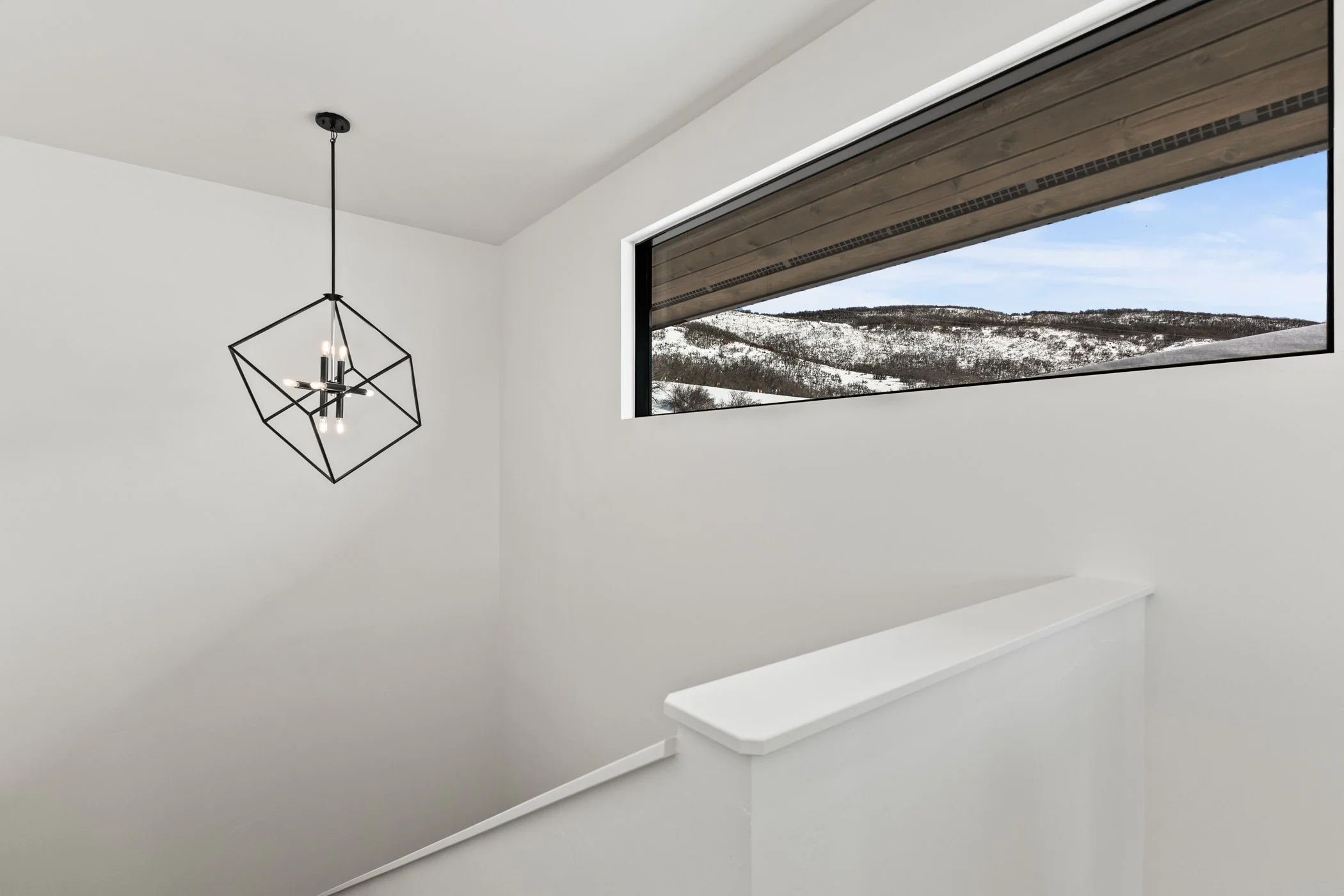 Modern staircase with geometric pendant light and large window showcasing snowy mountain view.