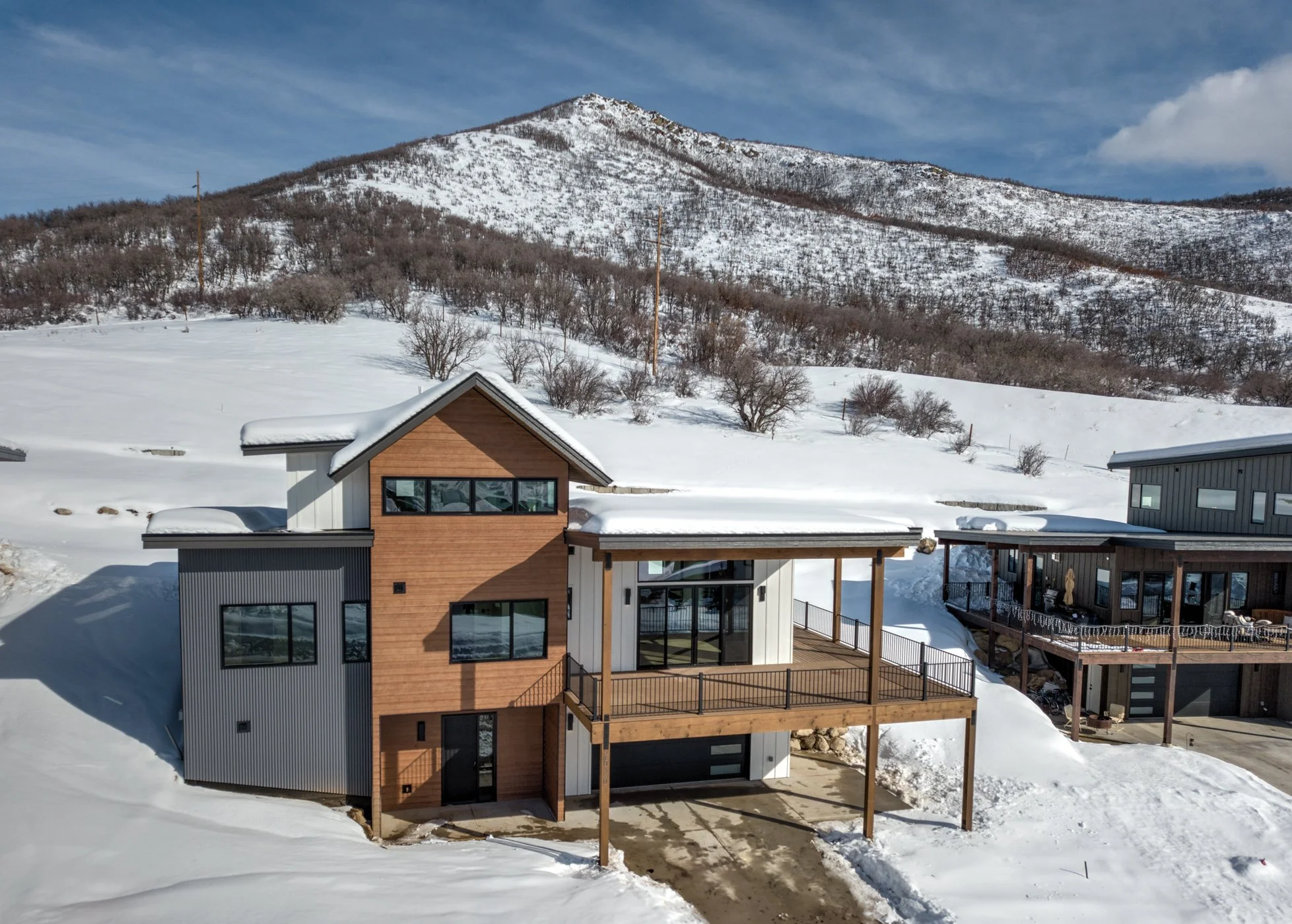 Modern house with wood and metal exterior surrounded by snow, with mountain backdrop.