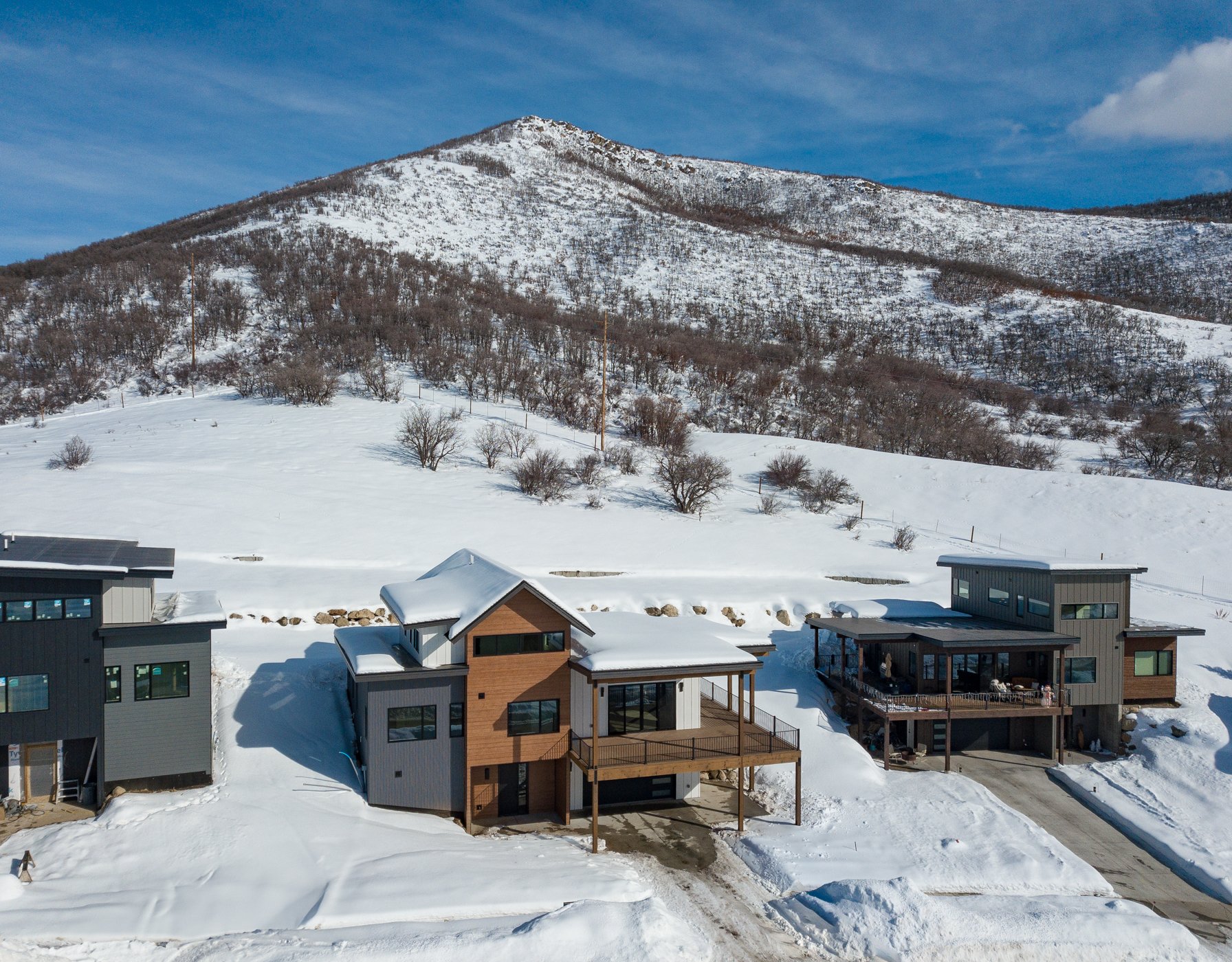Modern houses in snowy landscape with wooded hills in the background.