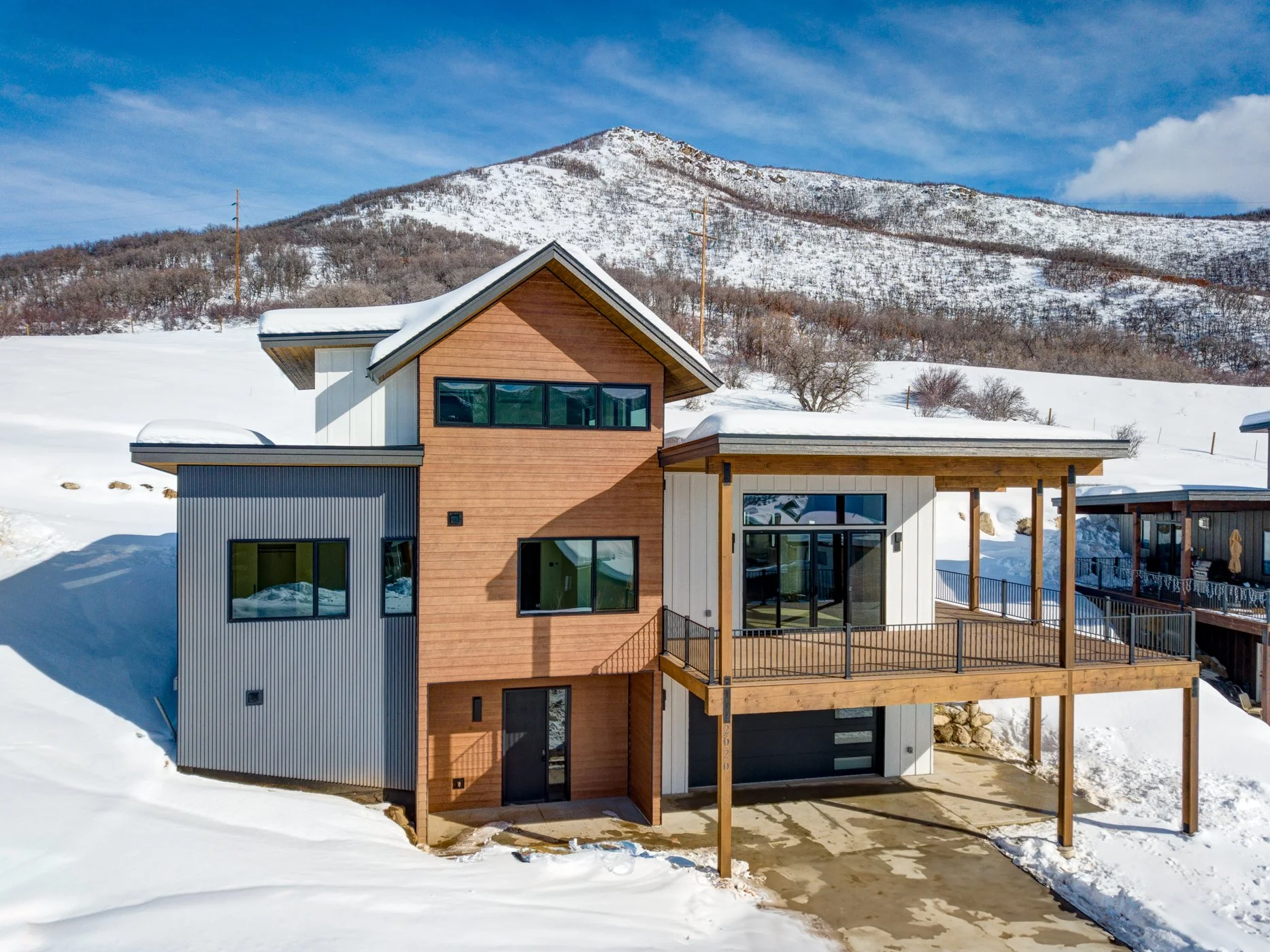 Modern house with wood and metal siding, snow-covered landscape, mountain background