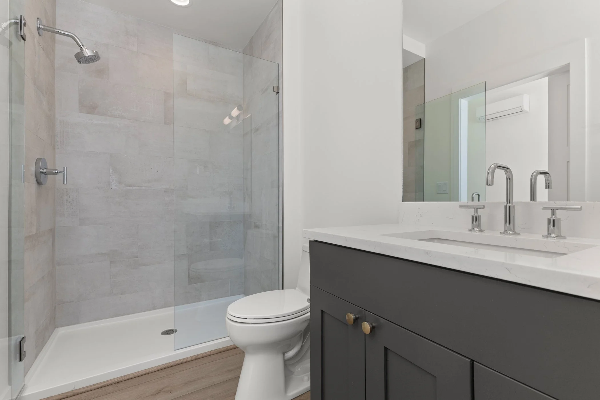 Modern bathroom with glass shower enclosure, white toilet, and dark vanity with dual sinks.