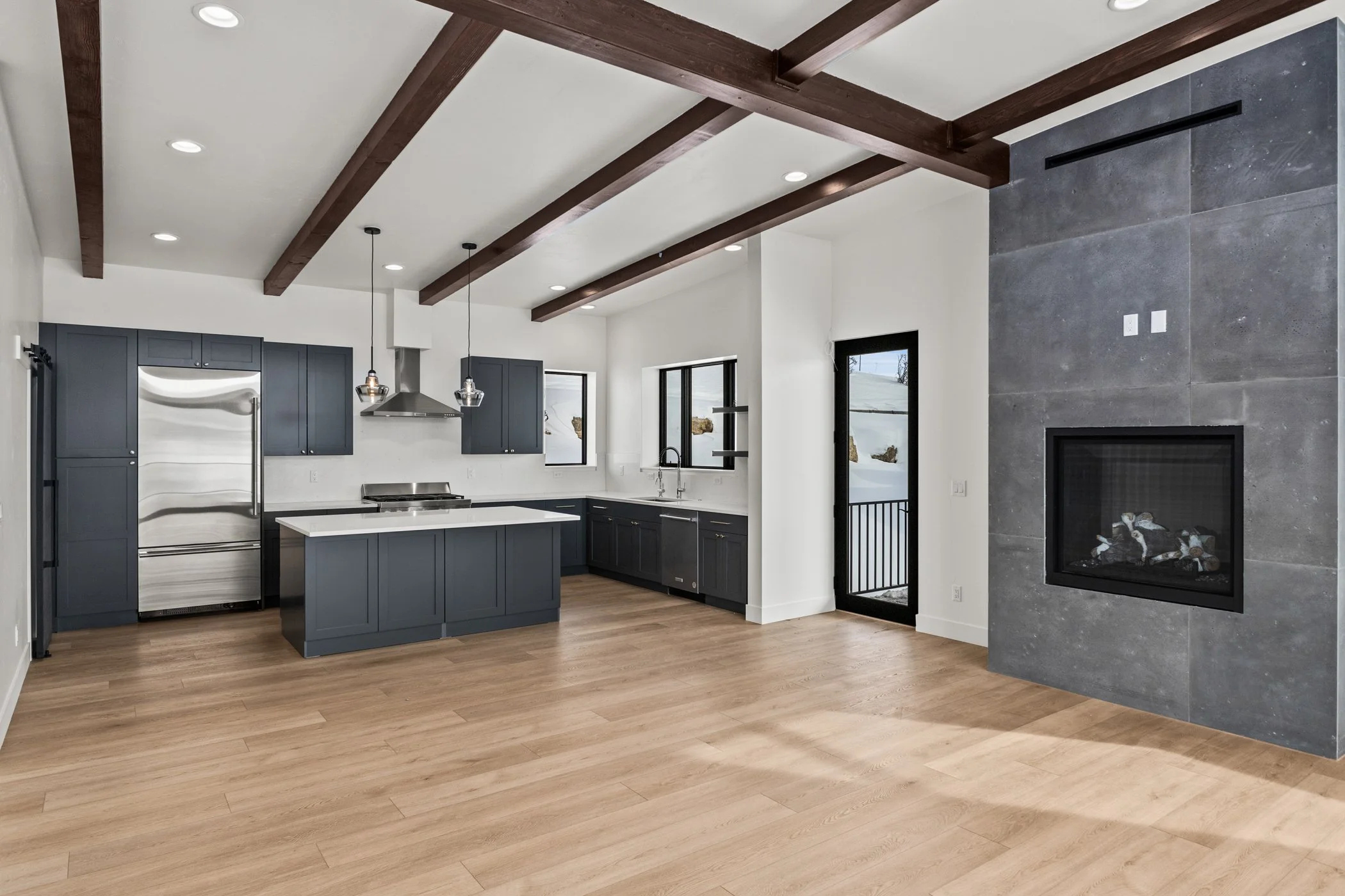Modern kitchen with hardwood floors, dark cabinets, stainless steel appliances, and a tiled fireplace wall.