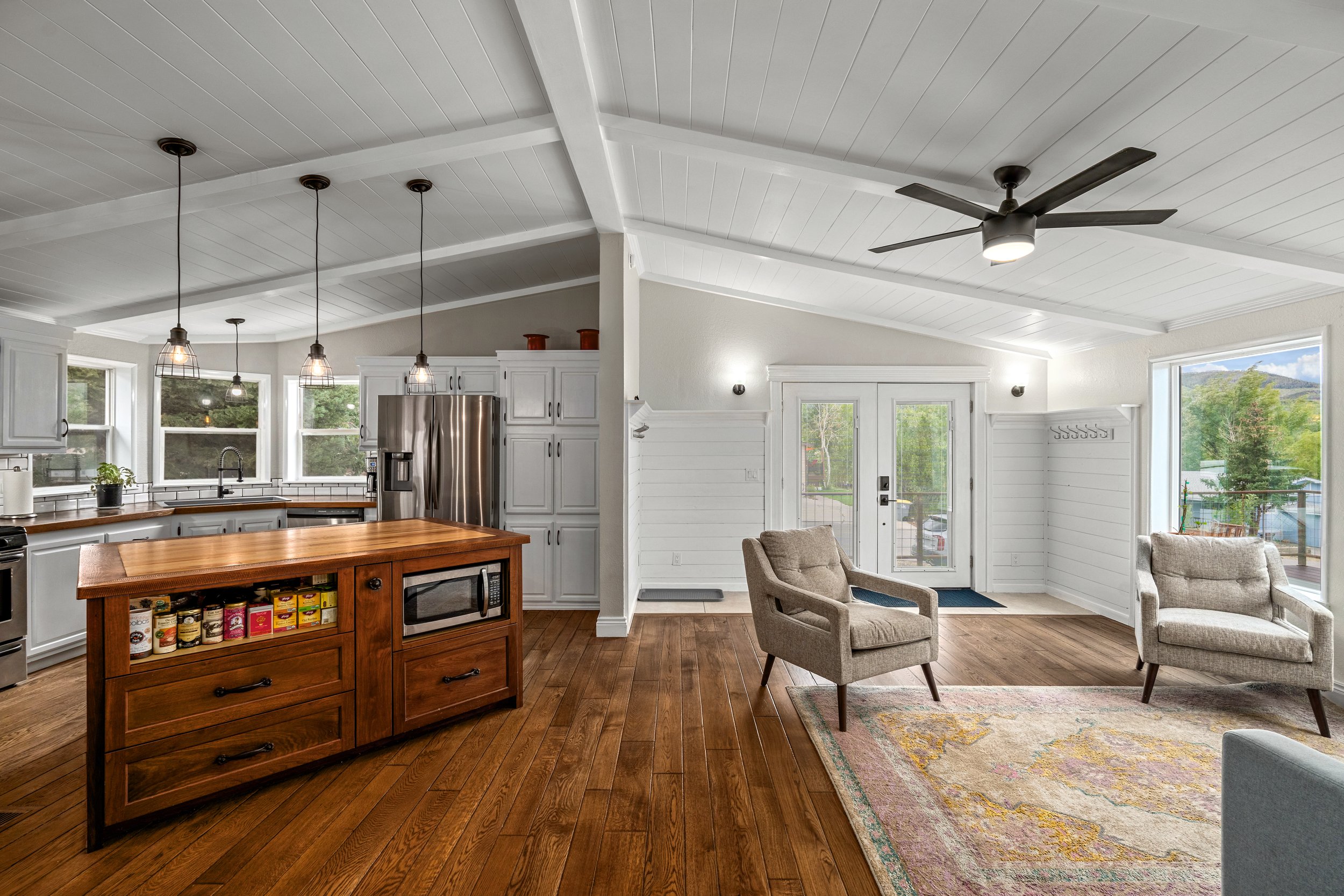 Open-concept kitchen and living area with white ceiling, wooden floors, center island, stainless steel appliances, and French doors.