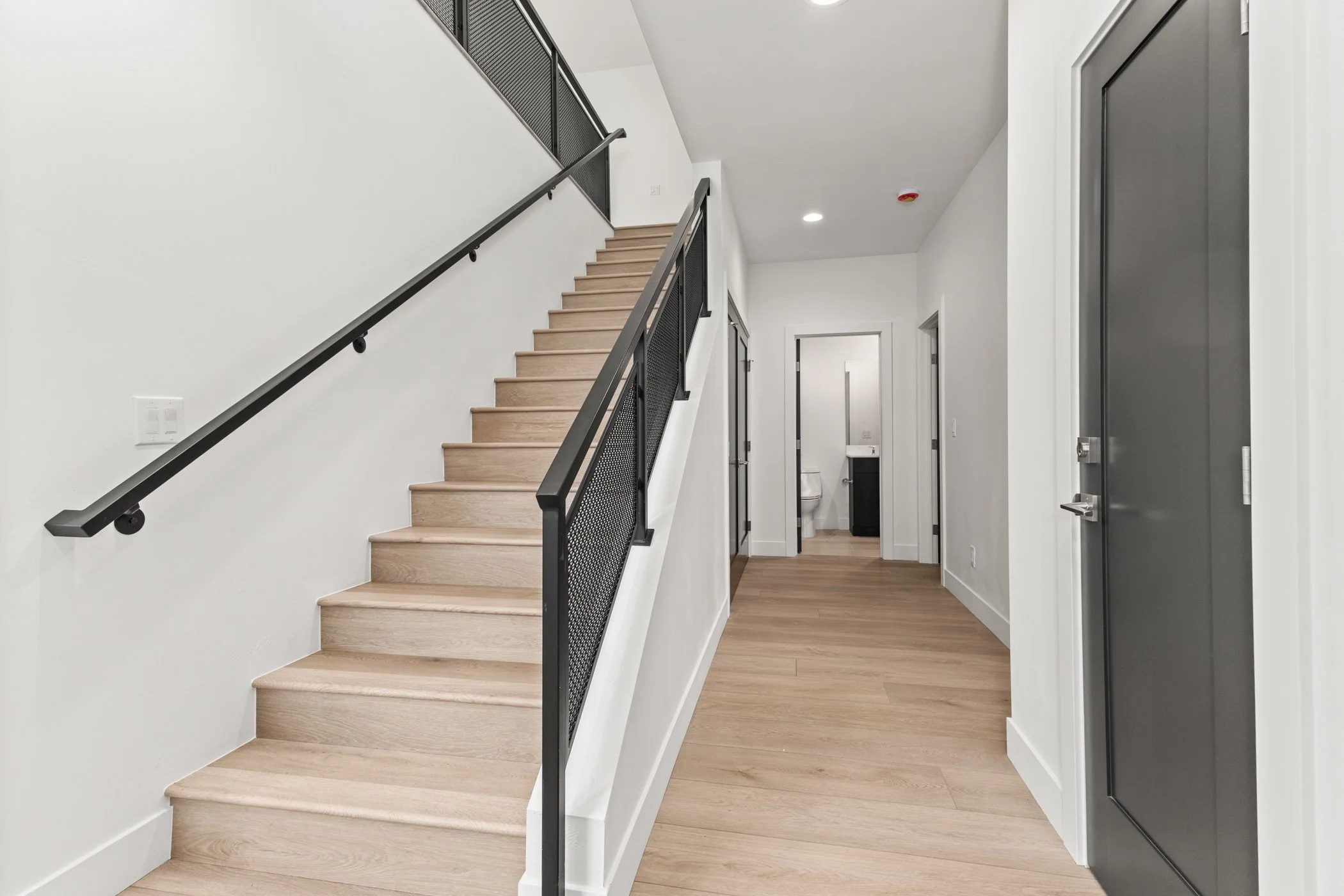 Modern indoor staircase with wooden steps and black metal railing in a hallway with wooden floor and doors.