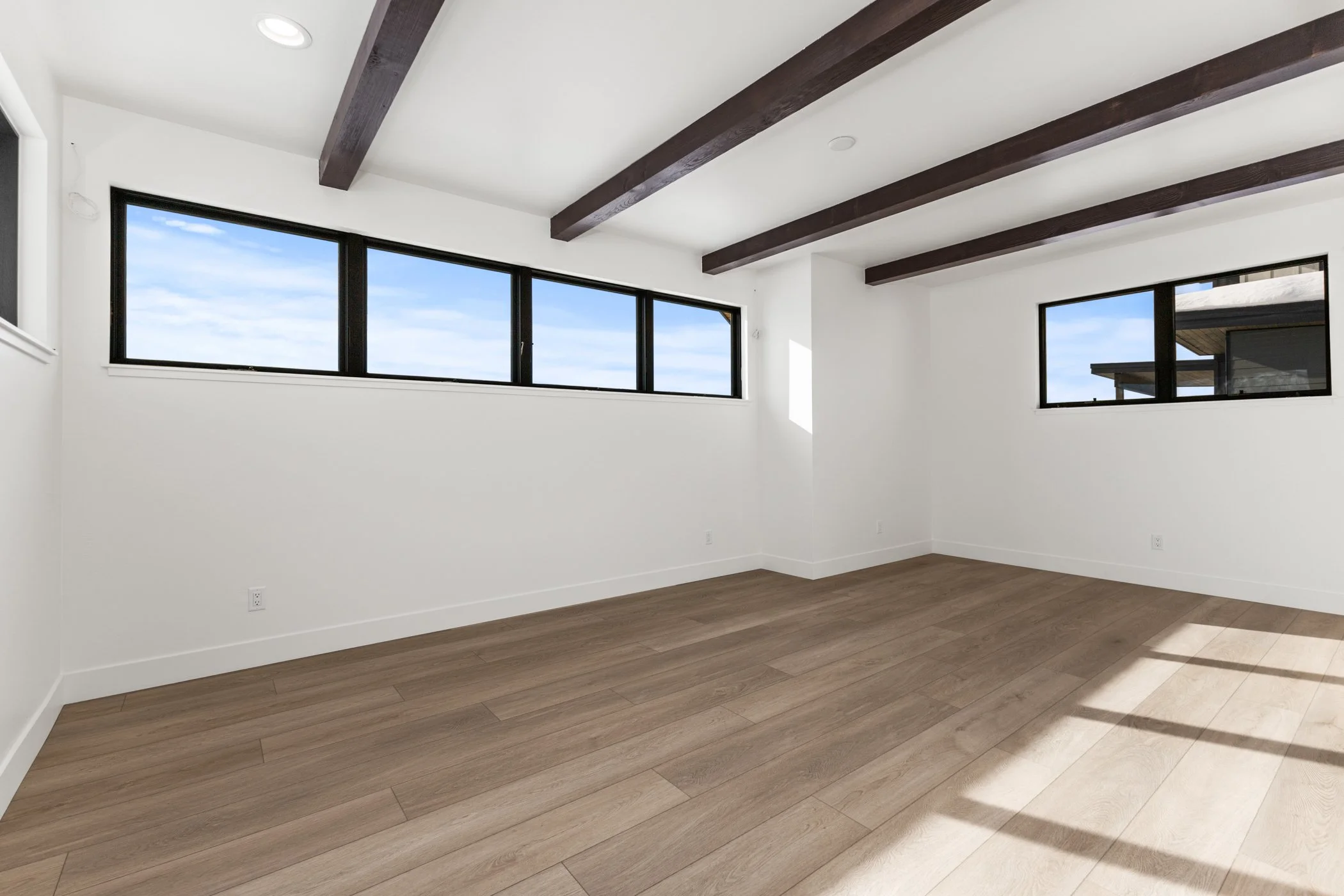 Empty room with white walls, wooden floor, and exposed dark ceiling beams.