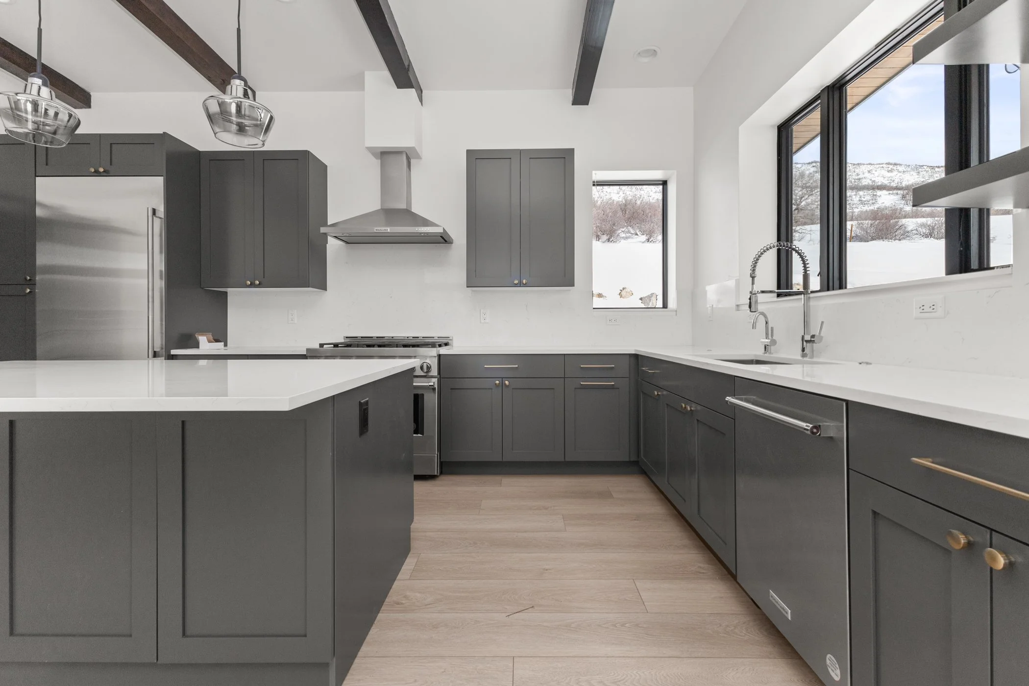 Modern kitchen with dark green cabinets, white countertops, stainless steel appliances, and light wooden floor.