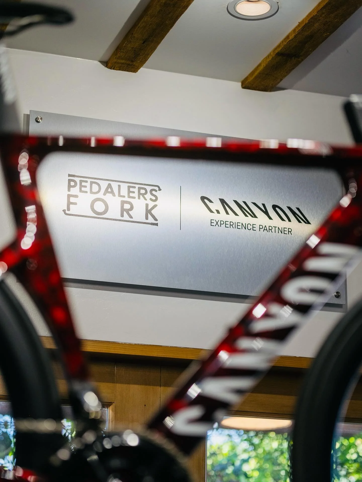 A bicycle frame in the foreground with a sign on the wall behind it reading 'Pedalers Fork' and 'Canyon Experience Partner.' Custom interior signage and point of sale display