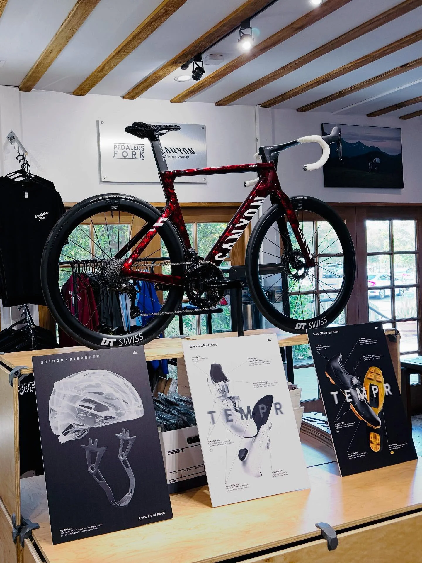 Custom interior signage and point of sale display. A red Cannondale bicycle mounted on a display shelf inside a store, with informational posters about cycling gear and accessories in front of it.
