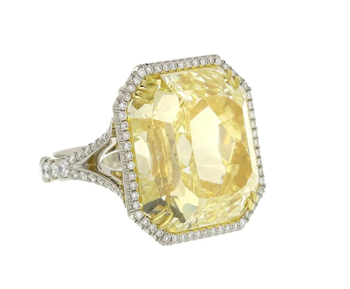 Large yellow gemstone ring with diamond accents on platinum band on white background.