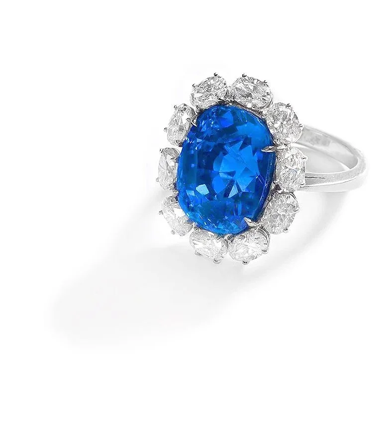 A silver ring featuring a large blue gemstone surrounded by smaller clear gemstones, placed on a white background.