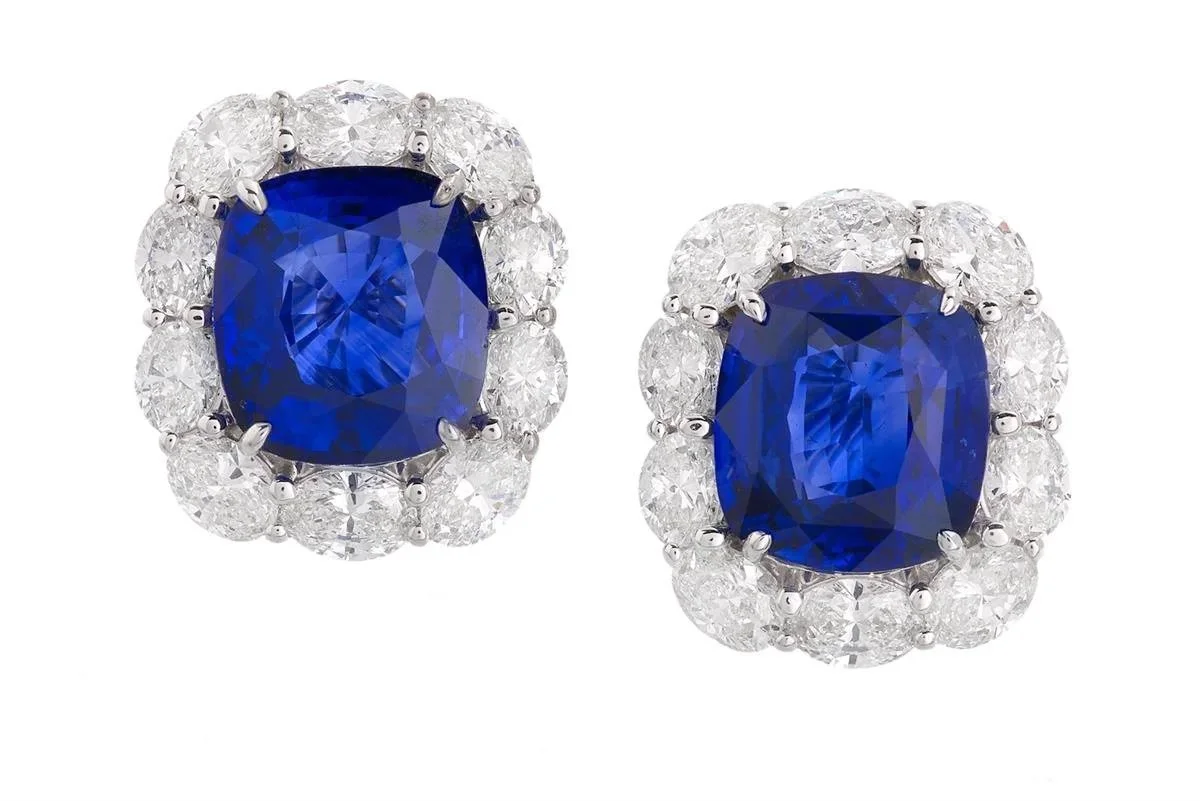 Pair of earrings featuring large blue sapphires surrounded by white diamonds on white background..