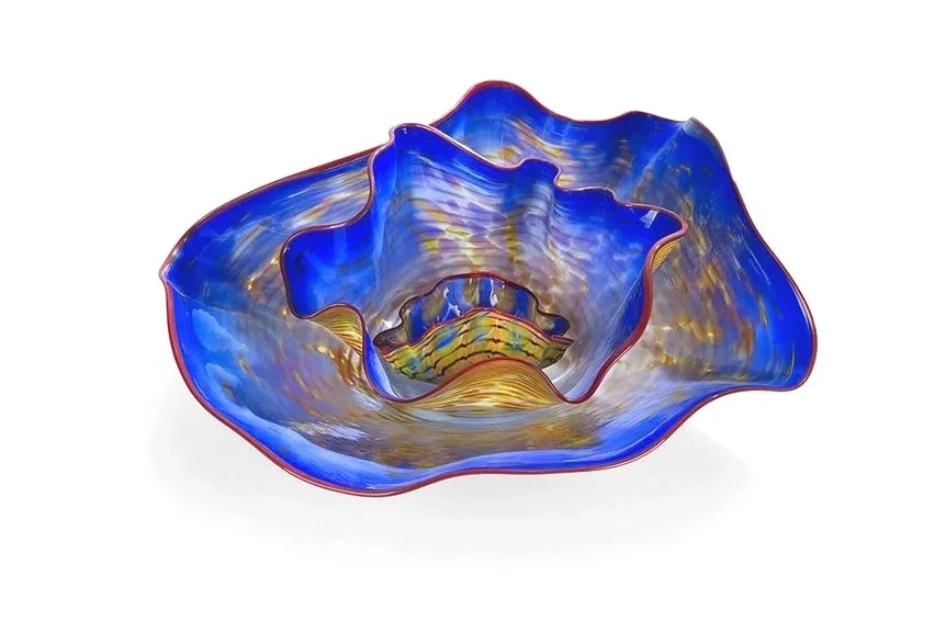 Chihuly blue and gold glass sculpture with wavy edges and red trim, resembling a flower or shell on white background.