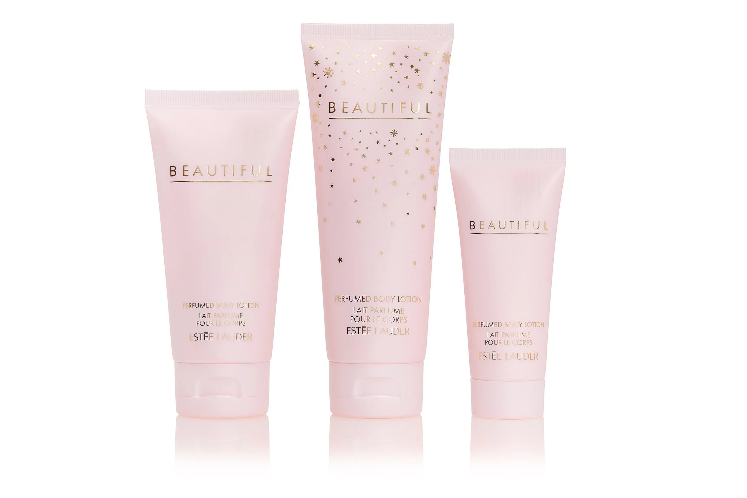 Three pink tubes of Estée Lauder perfume body lotion facing forward, with the middle tube slightly behind the others. The middle tube has gold star and snowflake designs and the word "BEAUTIFUL" printed on it.