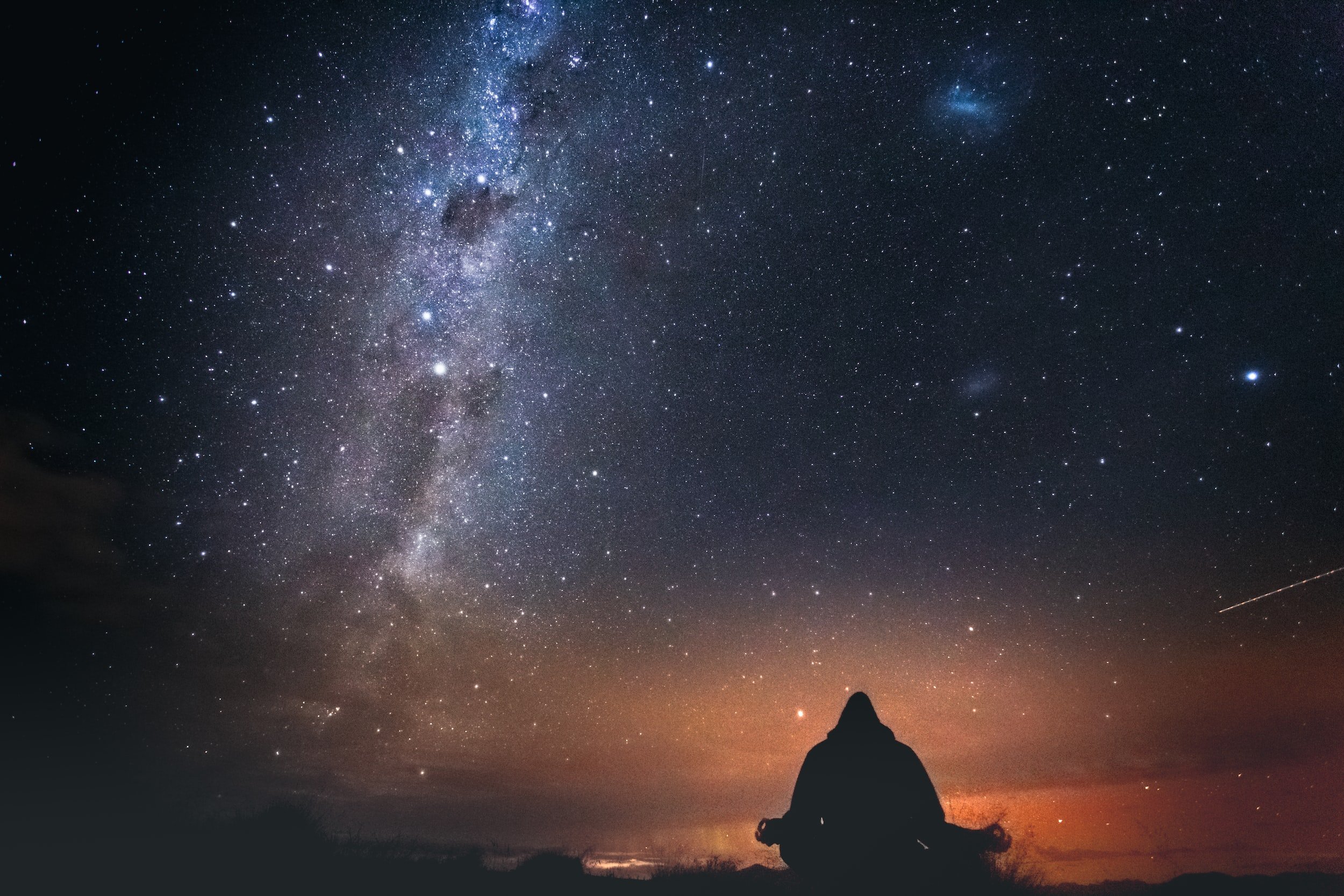 Silhouette of a person sitting outdoors at night, gazing at a starry sky with the Milky Way galaxy visible.