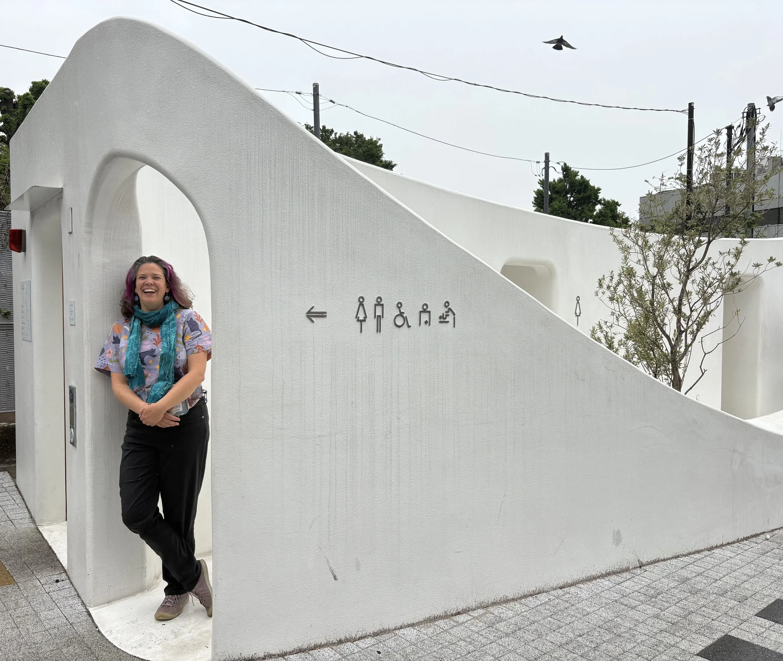 Katherine is leaning against the entrance to white public toilets.