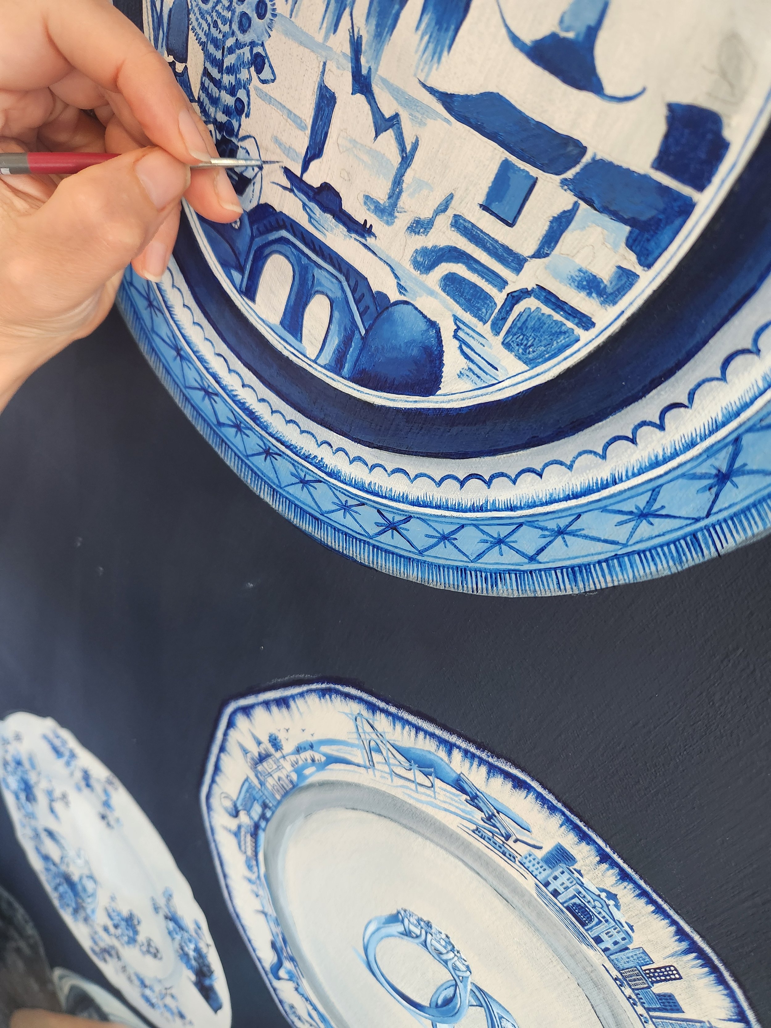 A person painting blue and white porcelain plates with intricate designs.