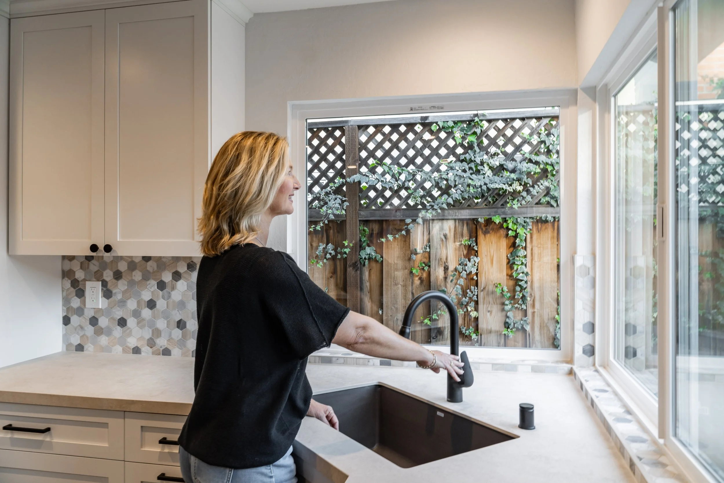 Designer Petra testing the matte black kitchen faucet at the sink in a bright, open-concept San Jose kitchen remodel.