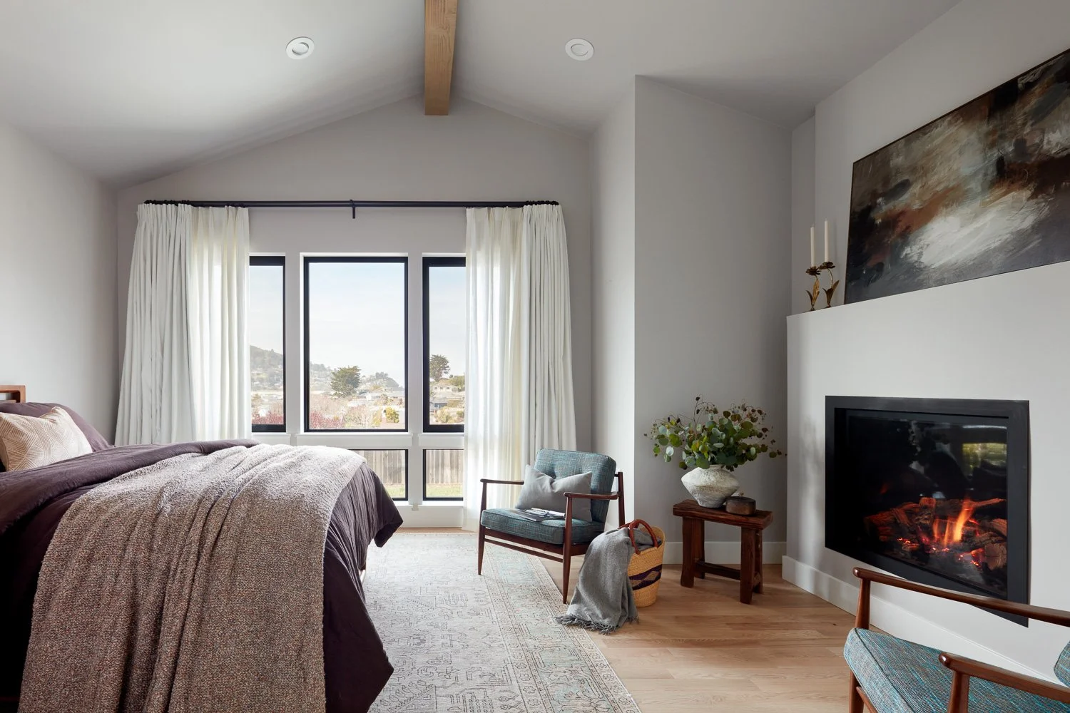 Primary bedroom retreat with vaulted ceilings, large windows, and cozy fireplace—designed for comfort, light, and coastal living.