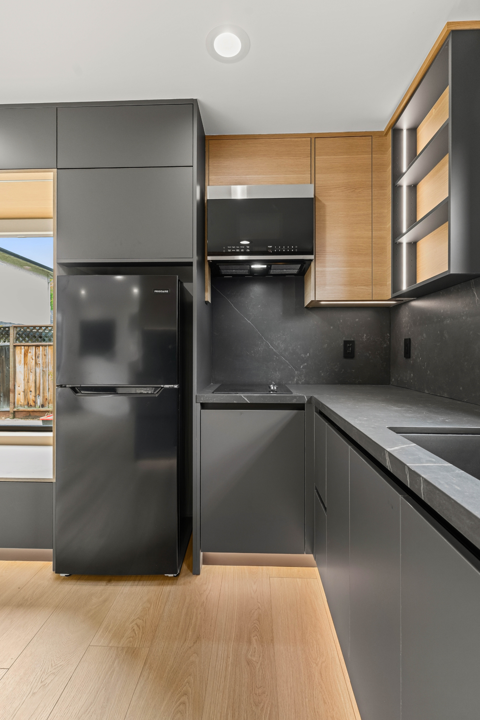 Modern ADU kitchen with custom cabinetry, quartz countertops, integrated lighting, and sleek black appliances.