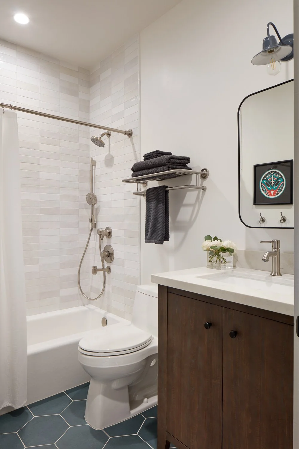 Guest bathroom with wood vanity, white tile tub surround, hex tile floor, and modern fixtures in Pacifica home remodel